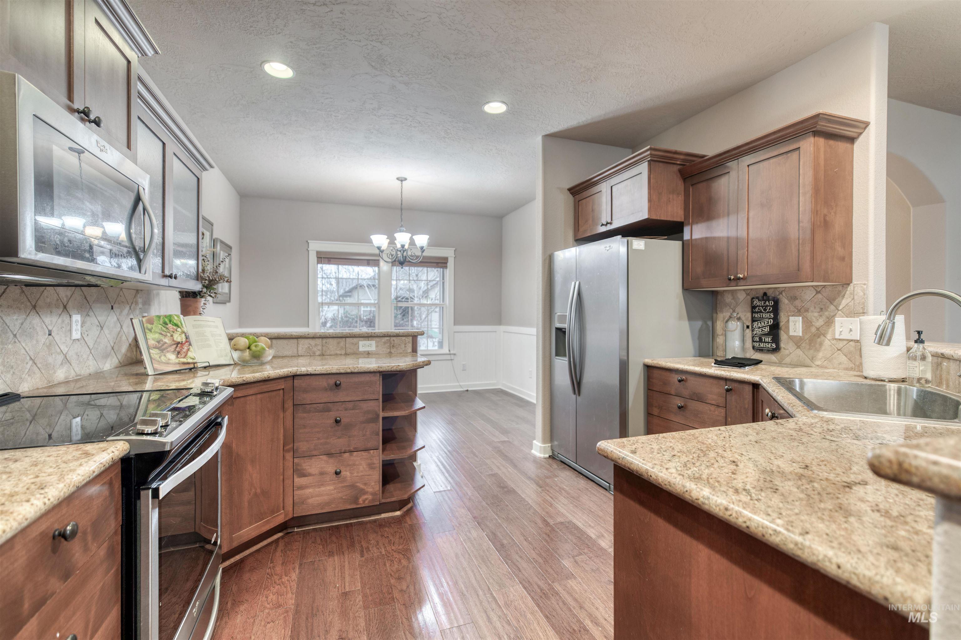 Kitchen with backsplash, appliances with stainless steel finishes, a peninsula, a textured ceiling, and light stone counters