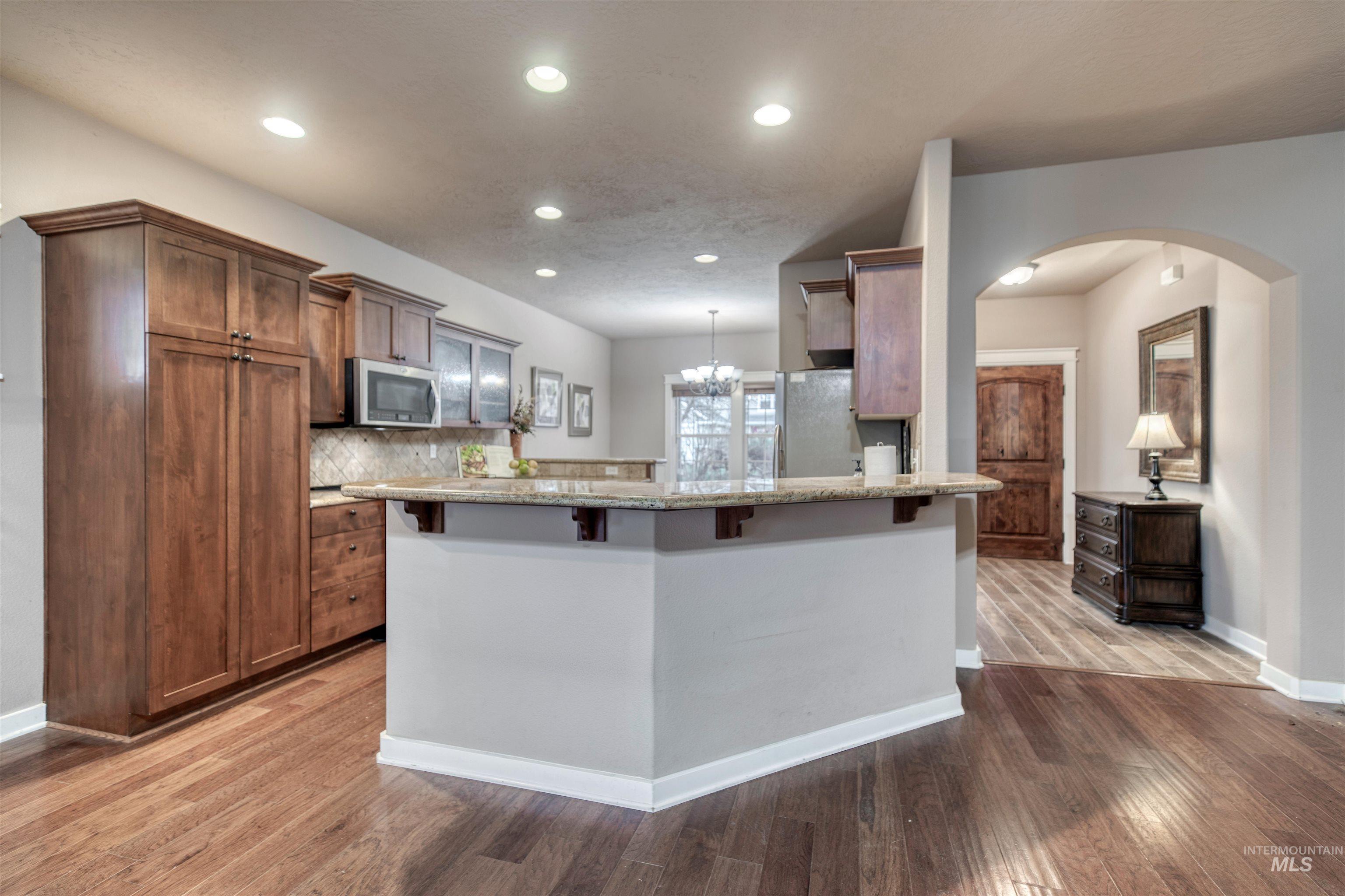 Kitchen featuring brown cabinetry, light stone counters, arched walkways, a peninsula, and light wood finished floors
