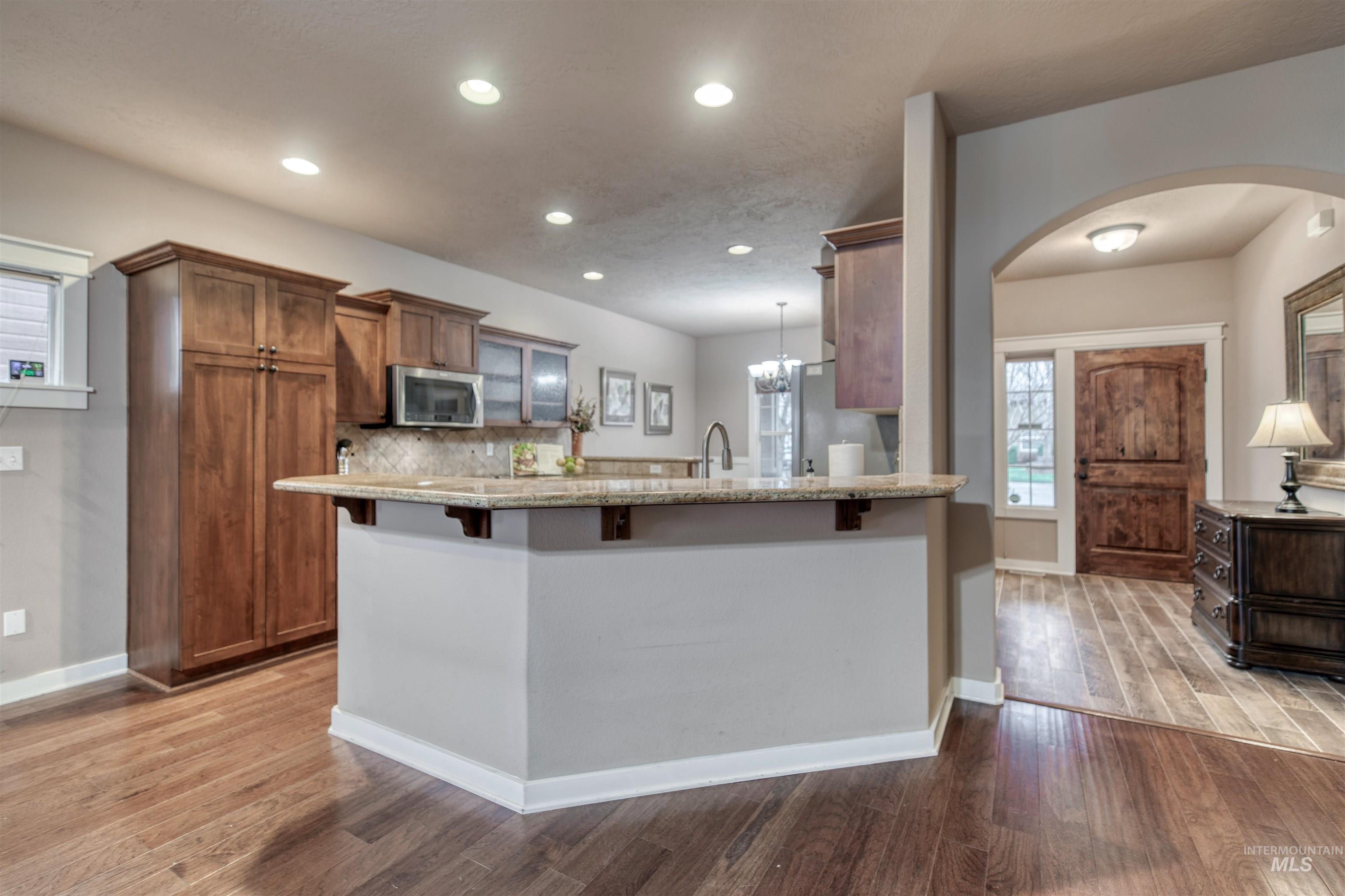 Kitchen featuring brown cabinetry, a breakfast bar, decorative light fixtures, light stone counters, and a peninsula