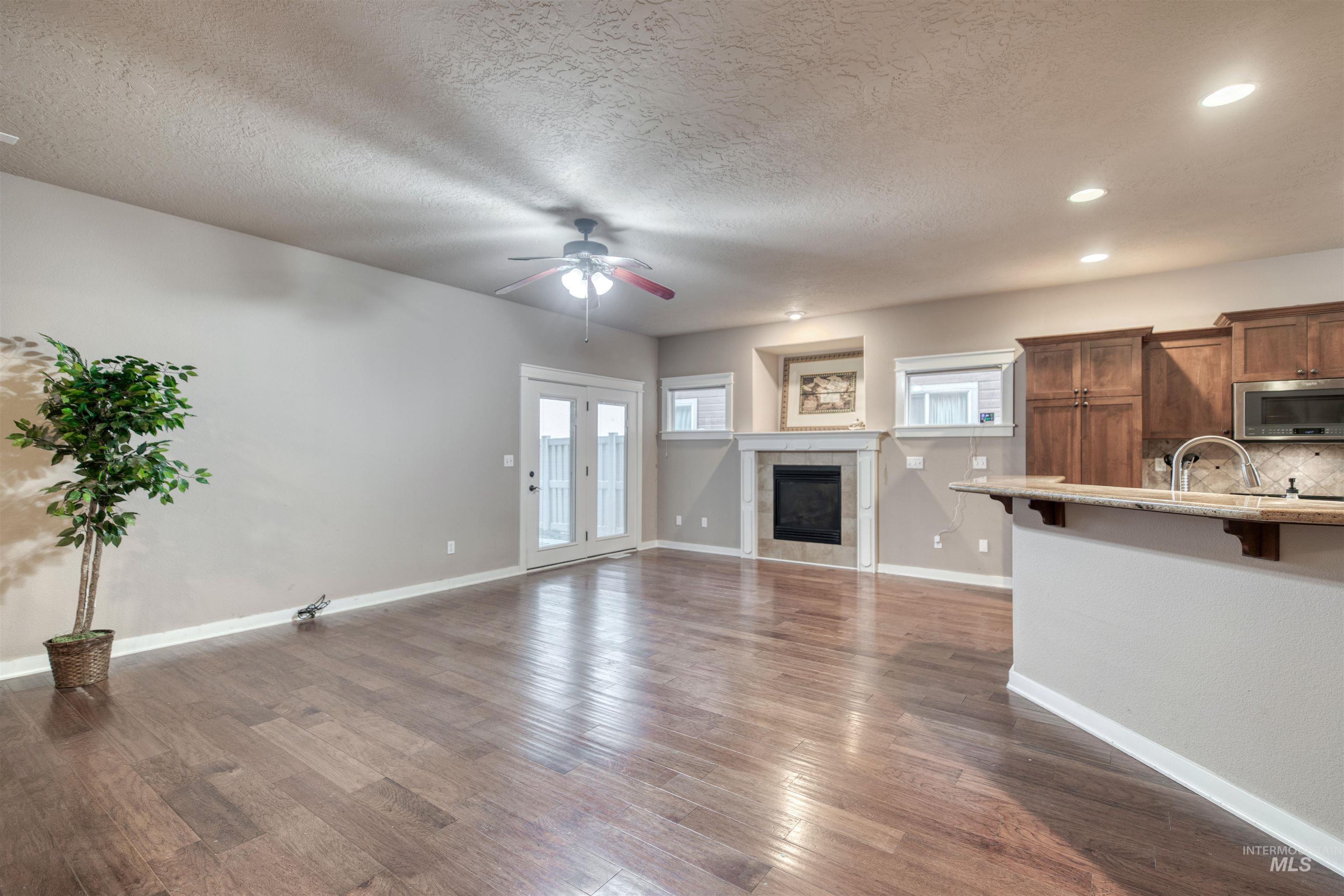 Unfurnished living room featuring a tiled fireplace, recessed lighting, wood finished floors, a textured ceiling, and ceiling fan