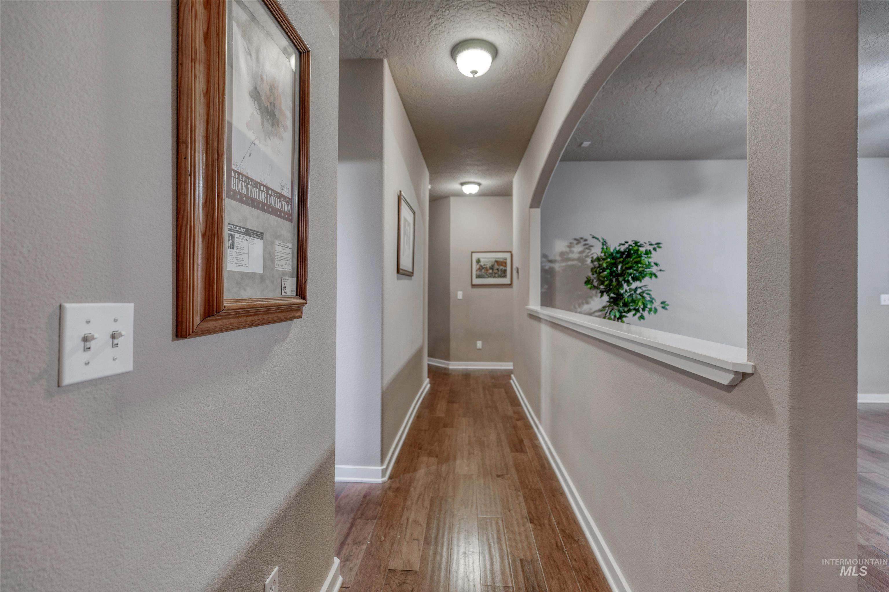 Corridor with light wood-type flooring, a textured ceiling, and a textured wall