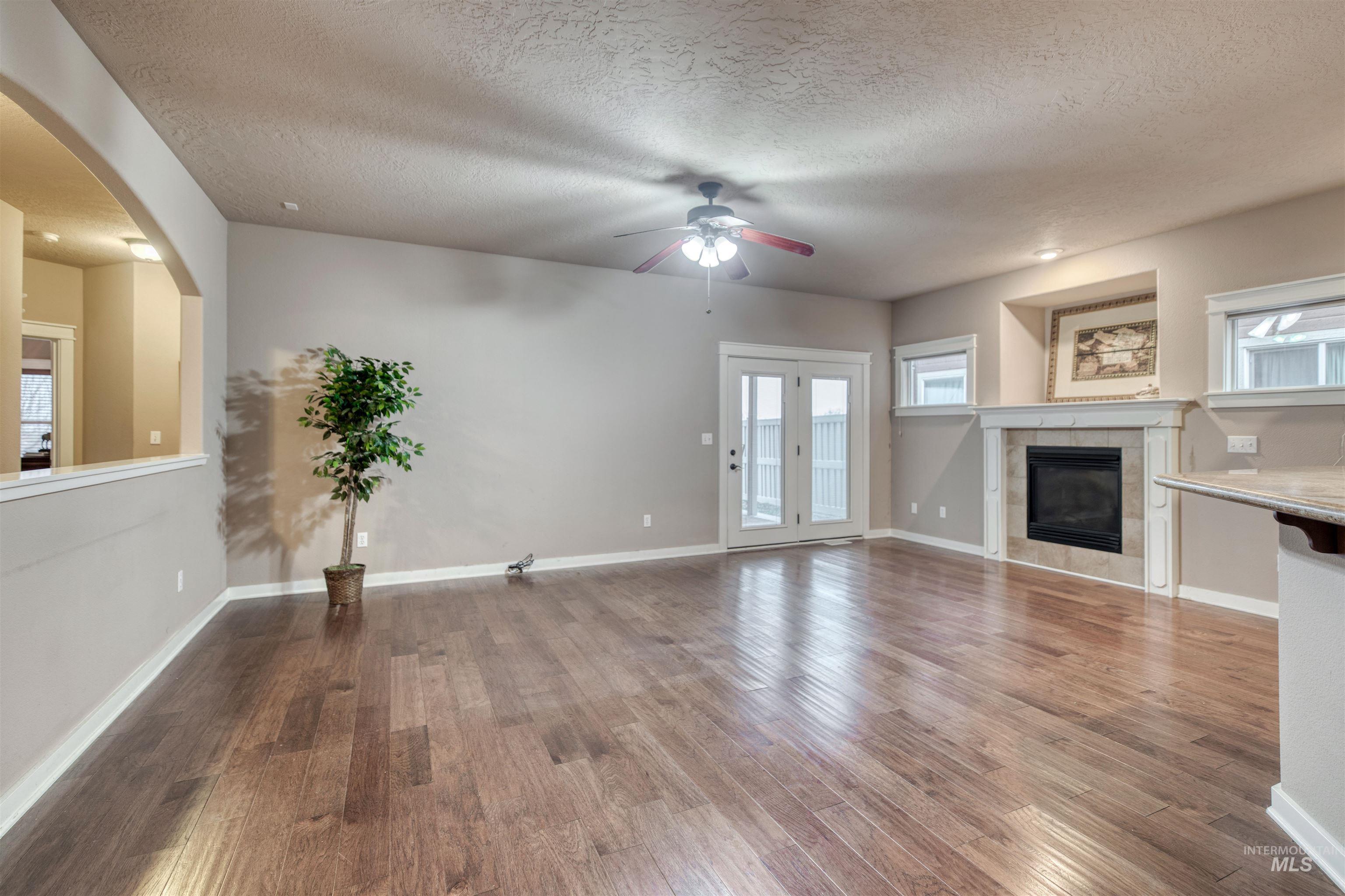 Unfurnished living room with a tile fireplace, a textured ceiling, light wood-style floors, arched walkways, and a ceiling fan