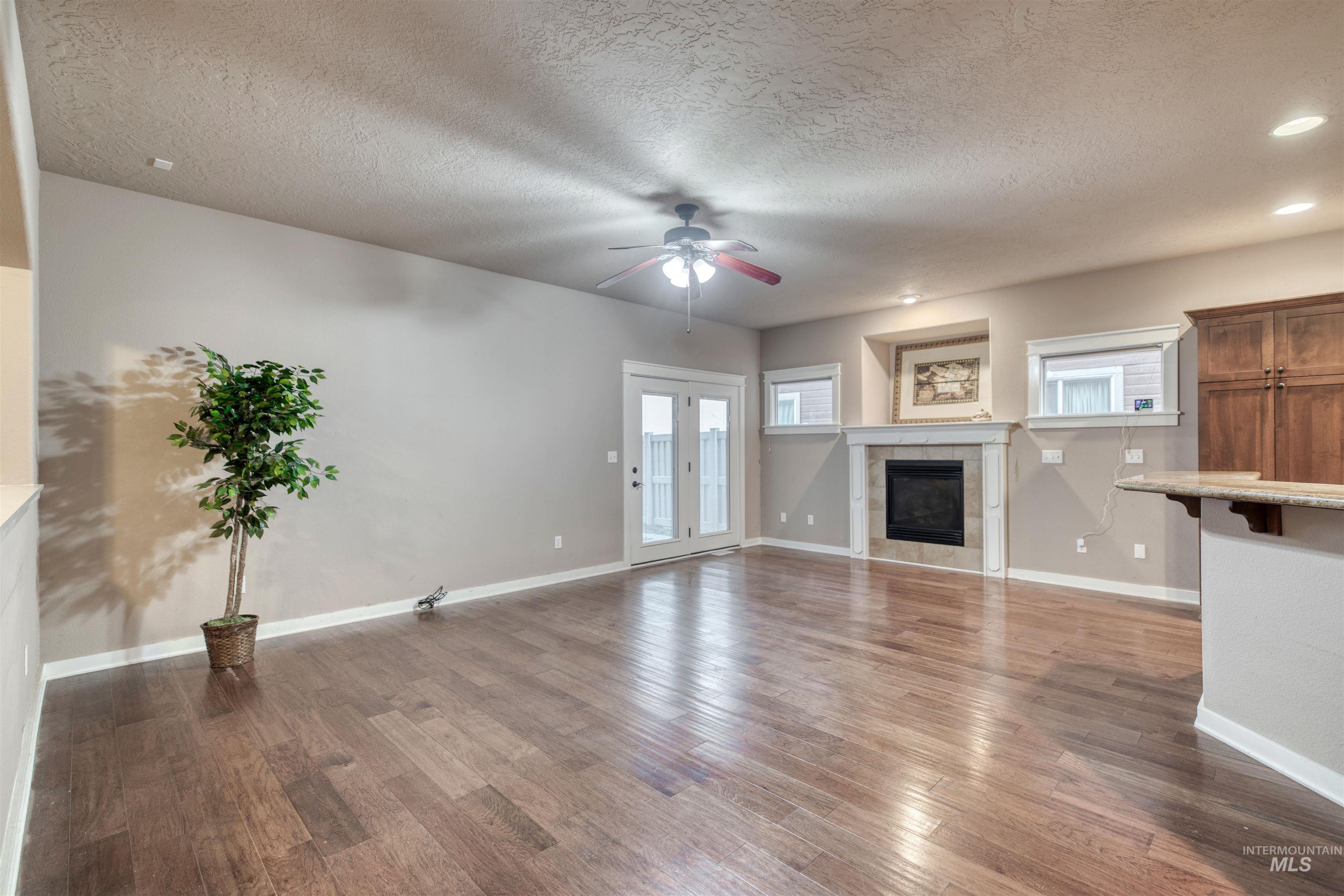 Unfurnished living room featuring a tile fireplace, wood finished floors, a textured ceiling, and a ceiling fan