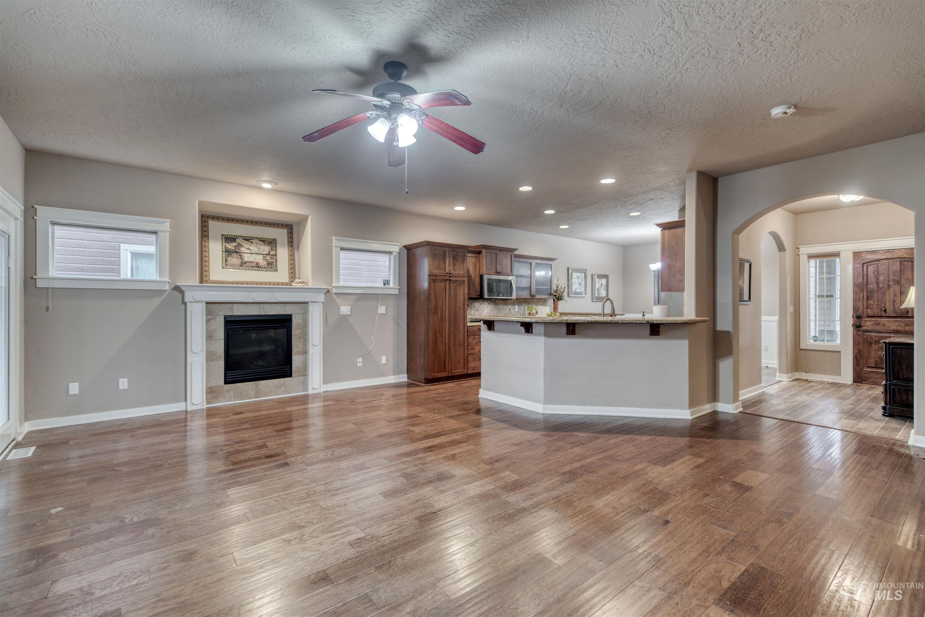 Unfurnished living room with a fireplace, ceiling fan, recessed lighting, light wood-style flooring, and arched walkways
