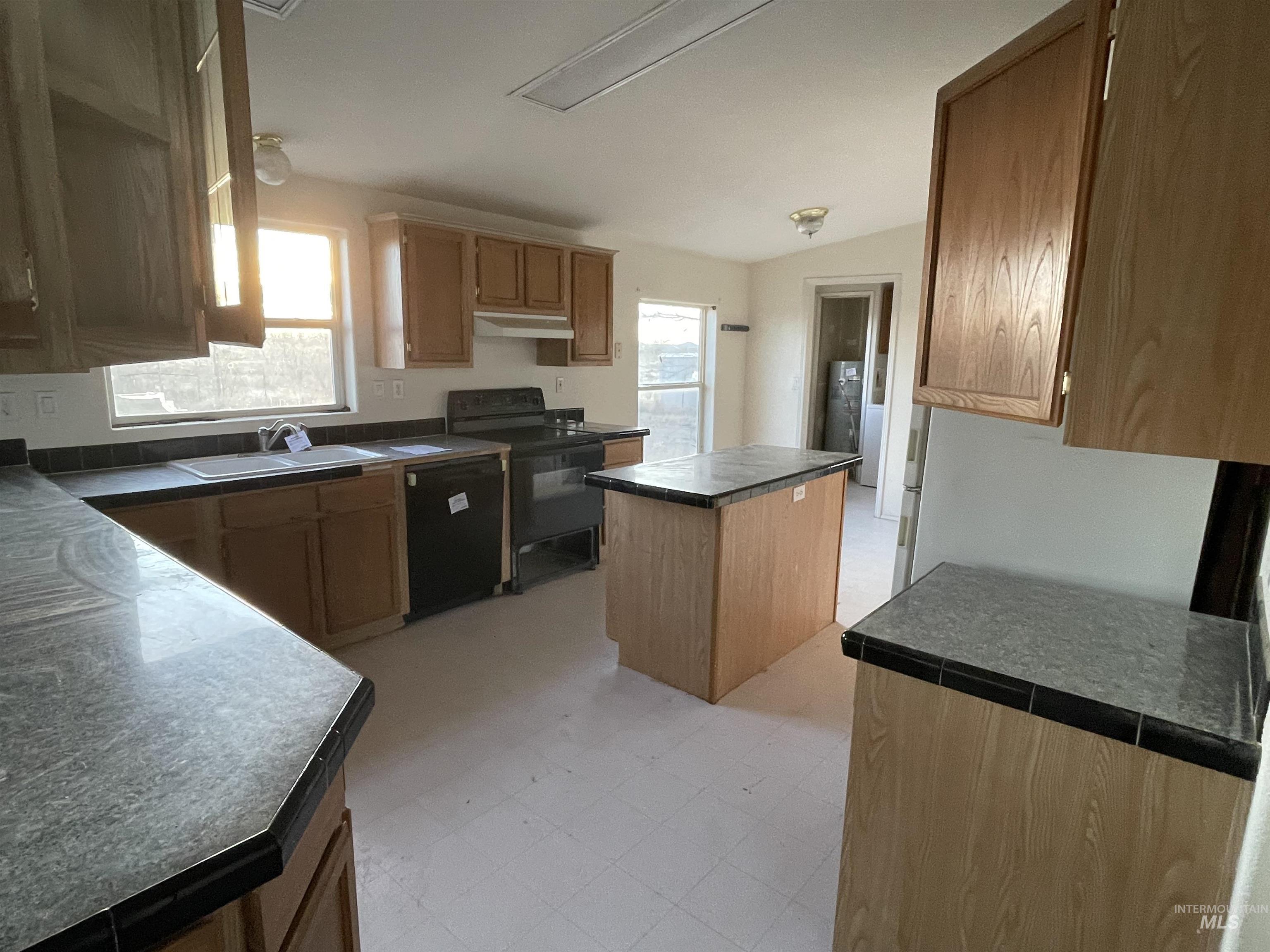 Kitchen with a kitchen island, dark countertops, black appliances, light floors, and under cabinet range hood