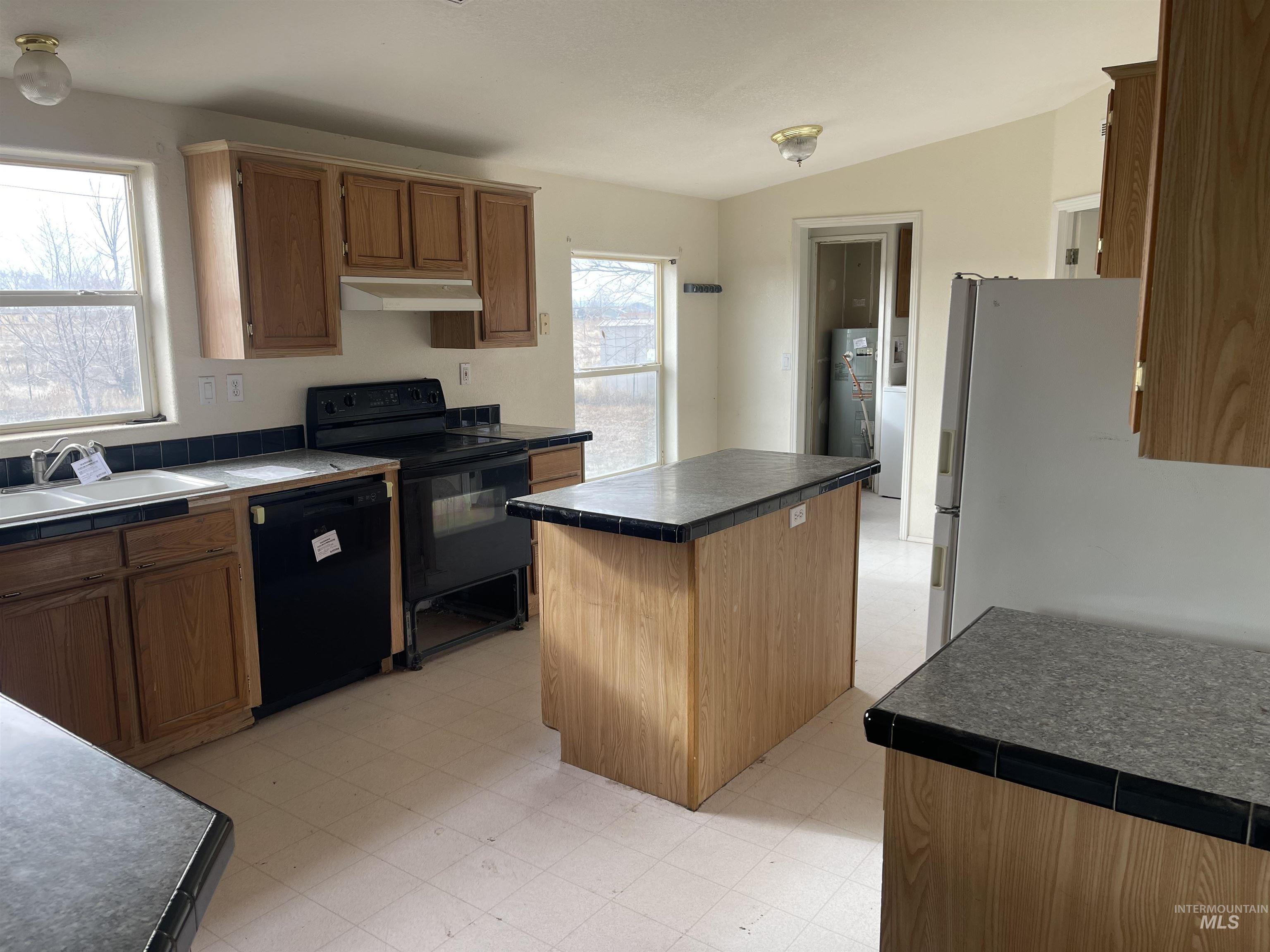Kitchen featuring light floors, black appliances, a center island, and tile countertops