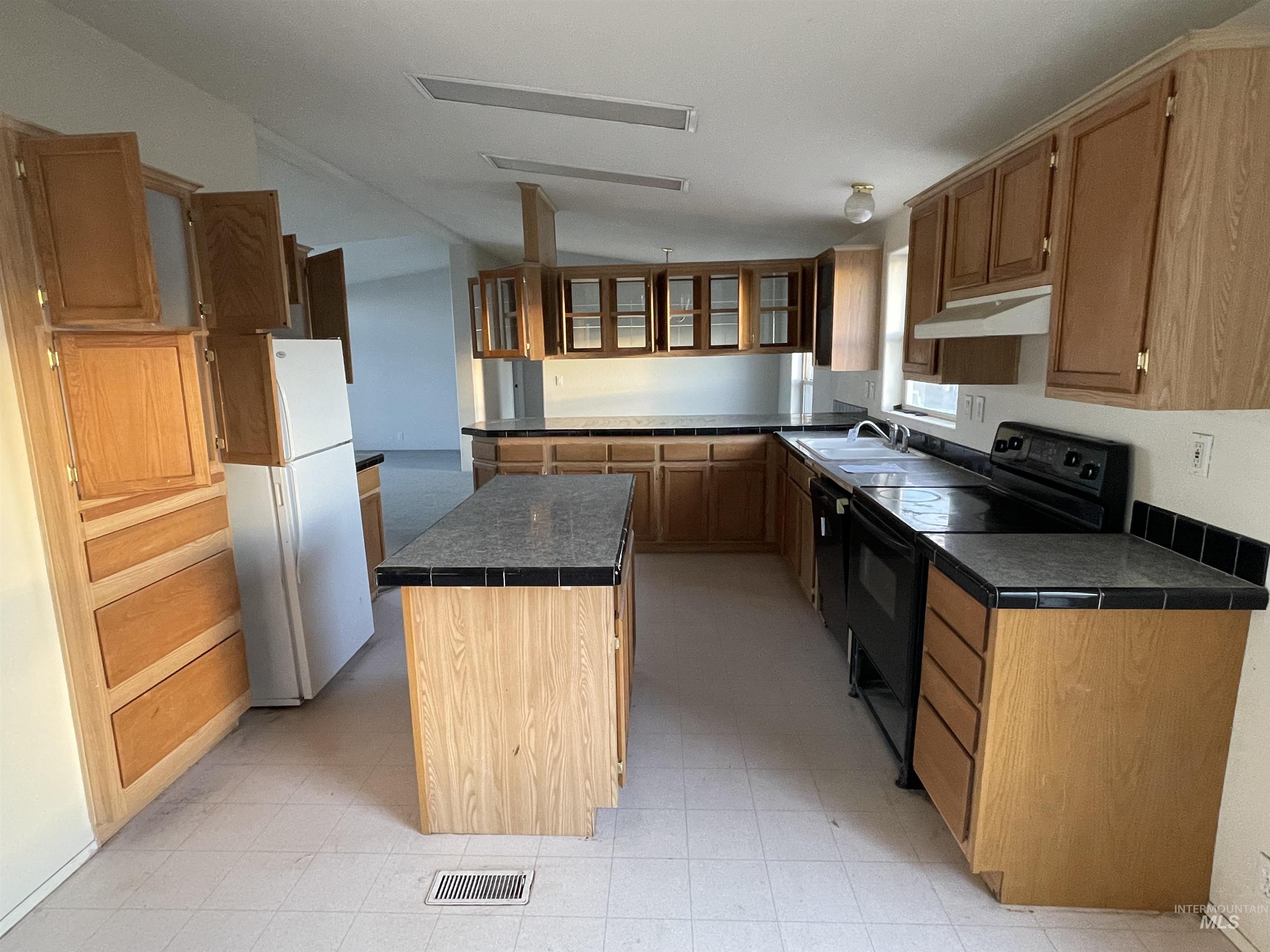 Kitchen featuring light floors, black appliances, dark countertops, a kitchen island, and vaulted ceiling