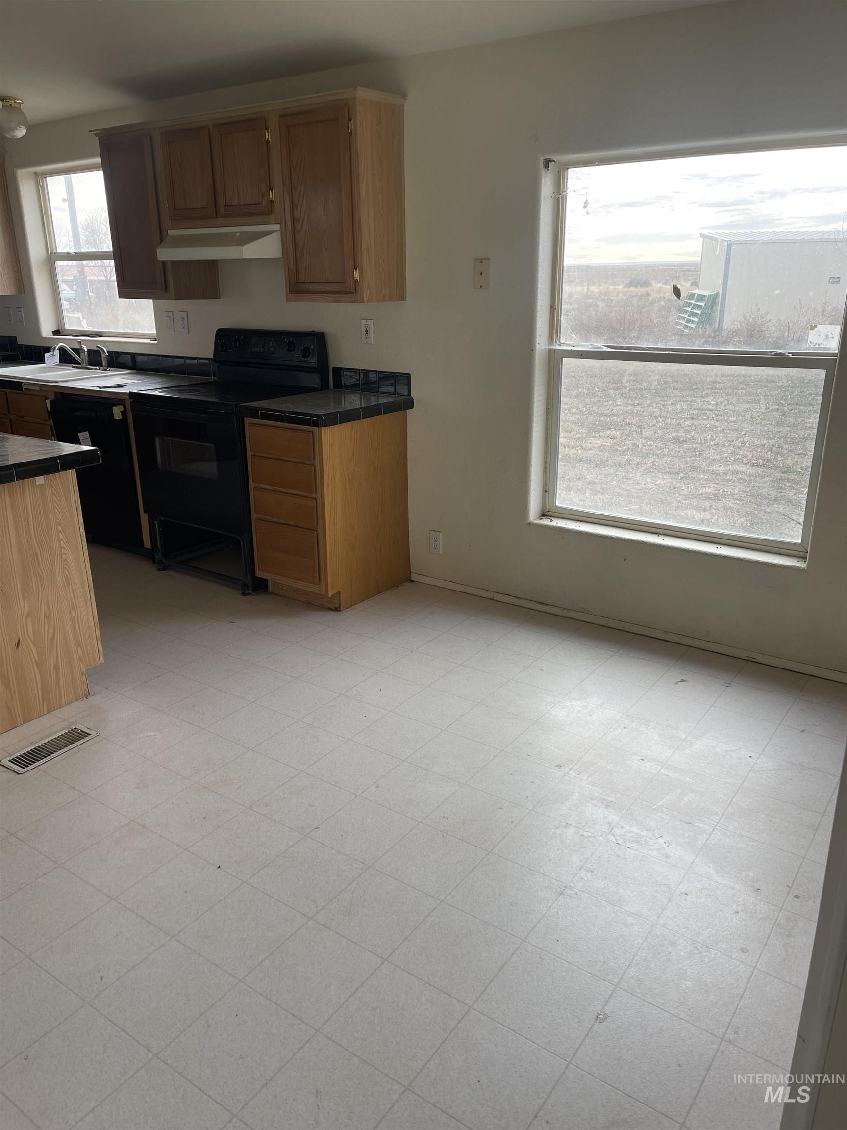 Kitchen with light flooring, tile countertops, and black appliances