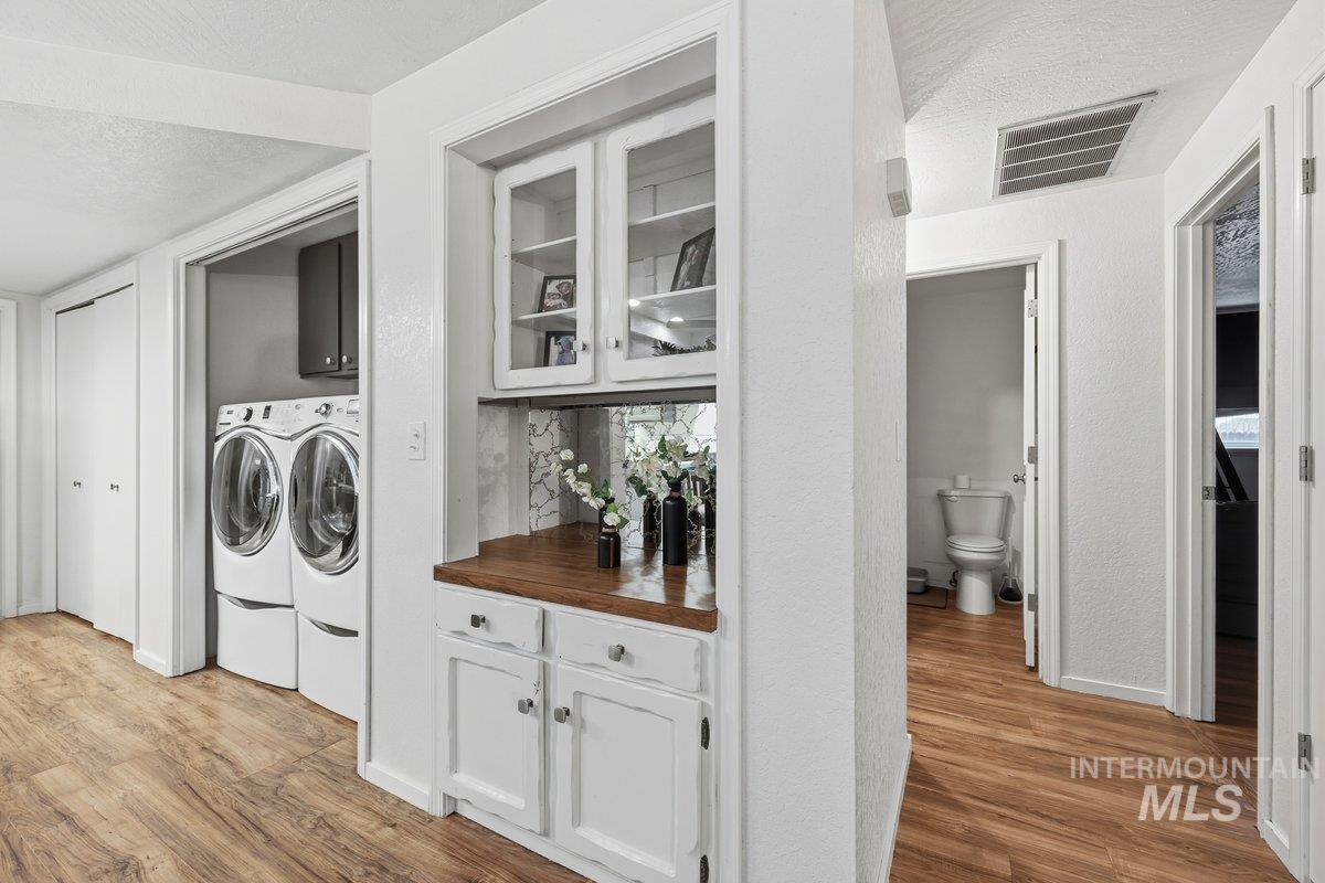 Laundry area featuring light wood-type flooring, a textured ceiling, washing machine and clothes dryer, and cabinet space