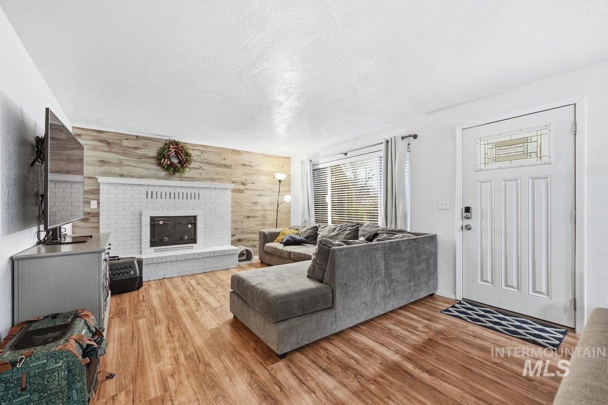 Living area featuring wooden walls, a textured ceiling, a brick fireplace, light wood finished floors, and an accent wall