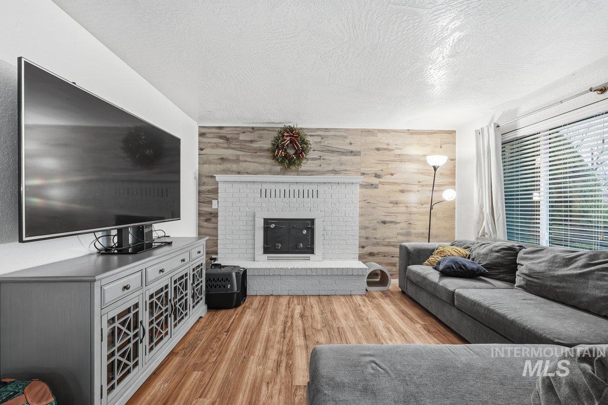 Living area featuring wood walls, light wood finished floors, a textured ceiling, and a brick fireplace