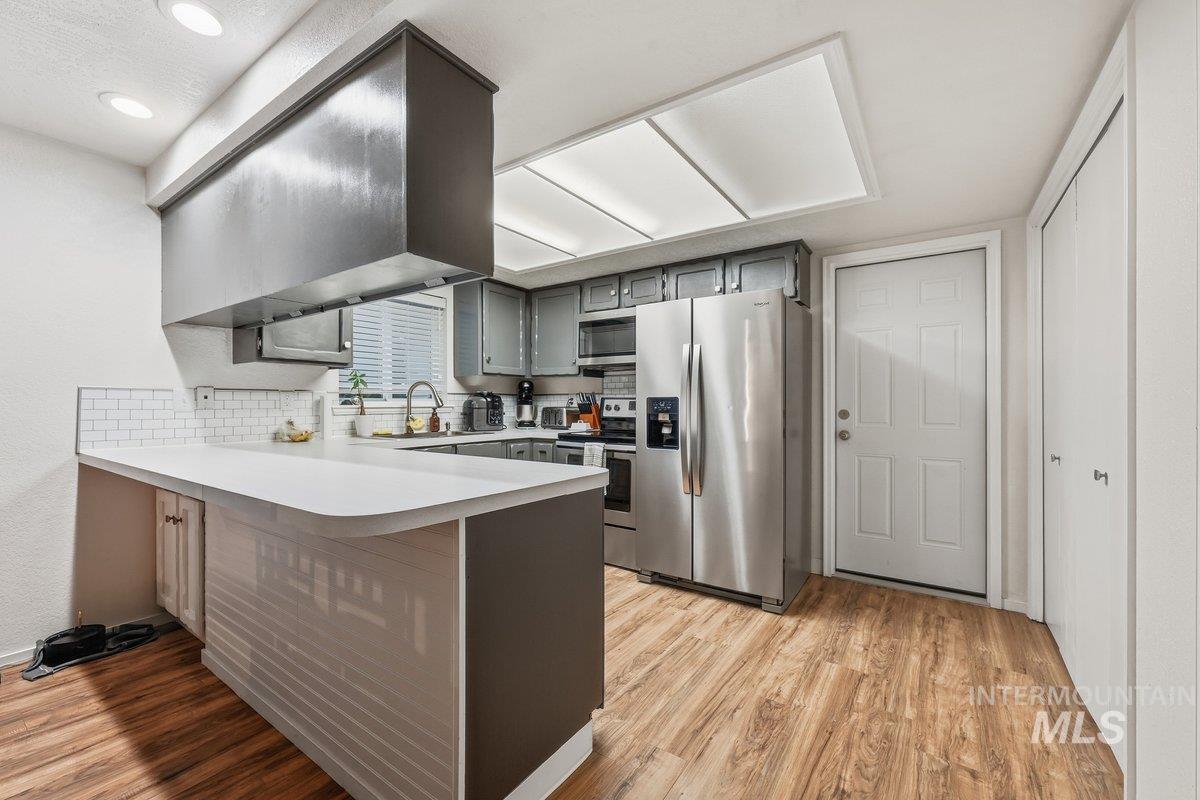 Kitchen with appliances with stainless steel finishes, light countertops, a peninsula, gray cabinets, and light wood-type flooring