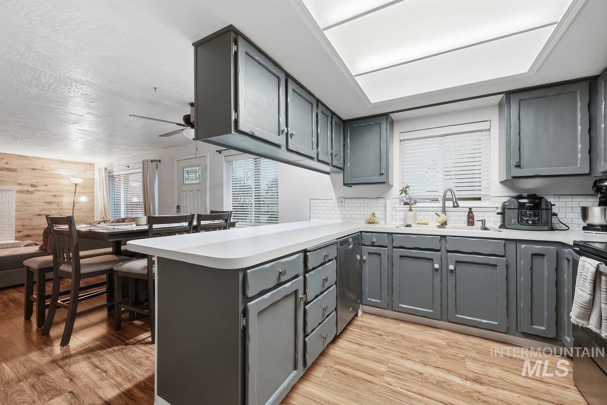 Kitchen with gray cabinets, a peninsula, light countertops, ceiling fan, and light wood-type flooring