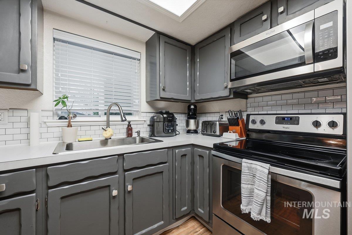 Kitchen with gray cabinets, appliances with stainless steel finishes, light countertops, and backsplash