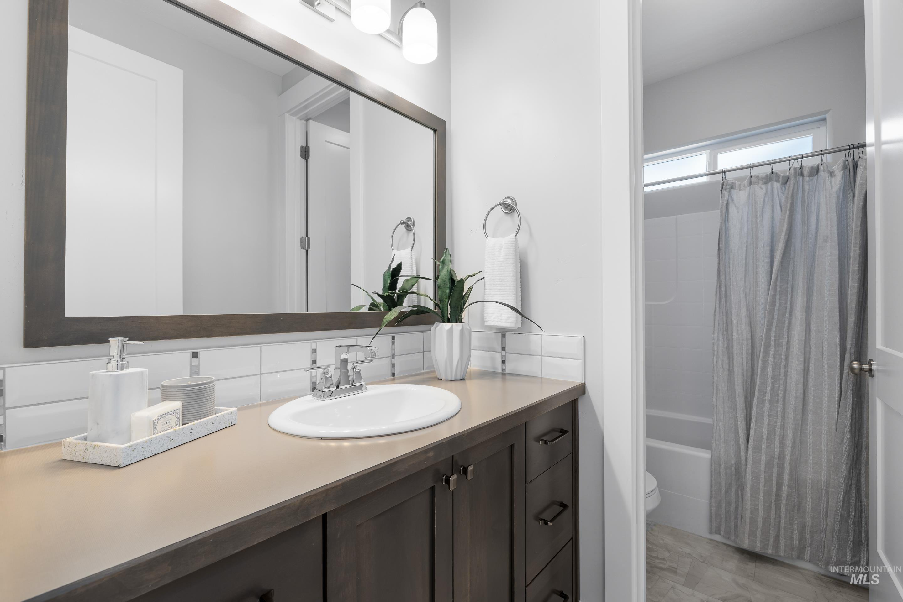 Bathroom featuring shower / bath combination with curtain, vanity, and decorative backsplash