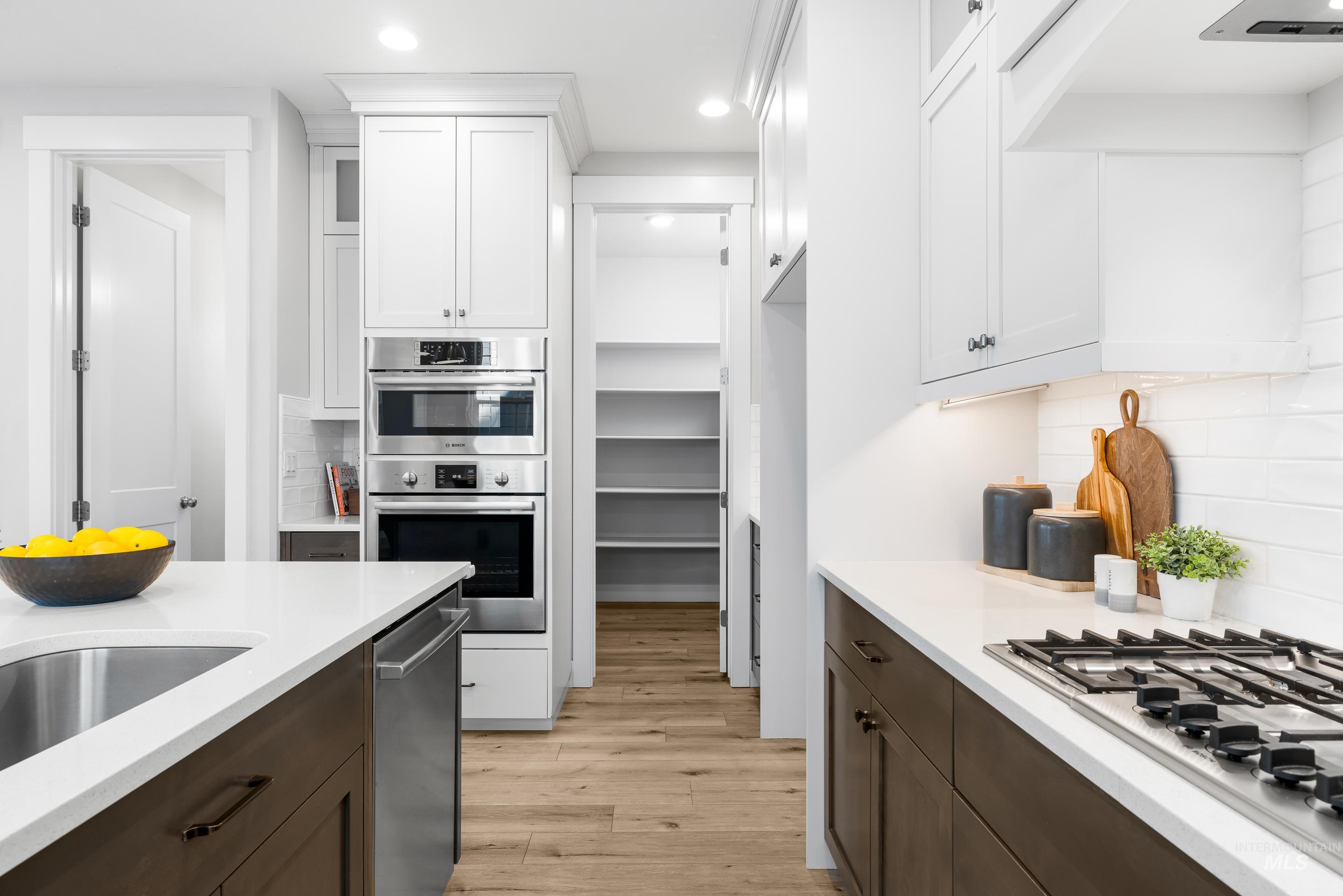 Kitchen featuring backsplash, dark brown cabinets, white cabinets, stainless steel appliances, and light wood-type flooring