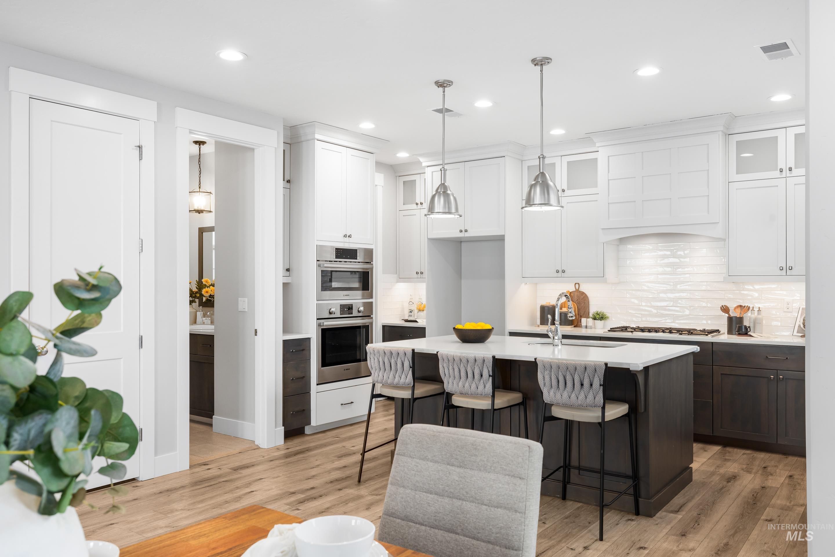 Kitchen with a breakfast bar area, backsplash, white cabinets, an island with sink, and recessed lighting