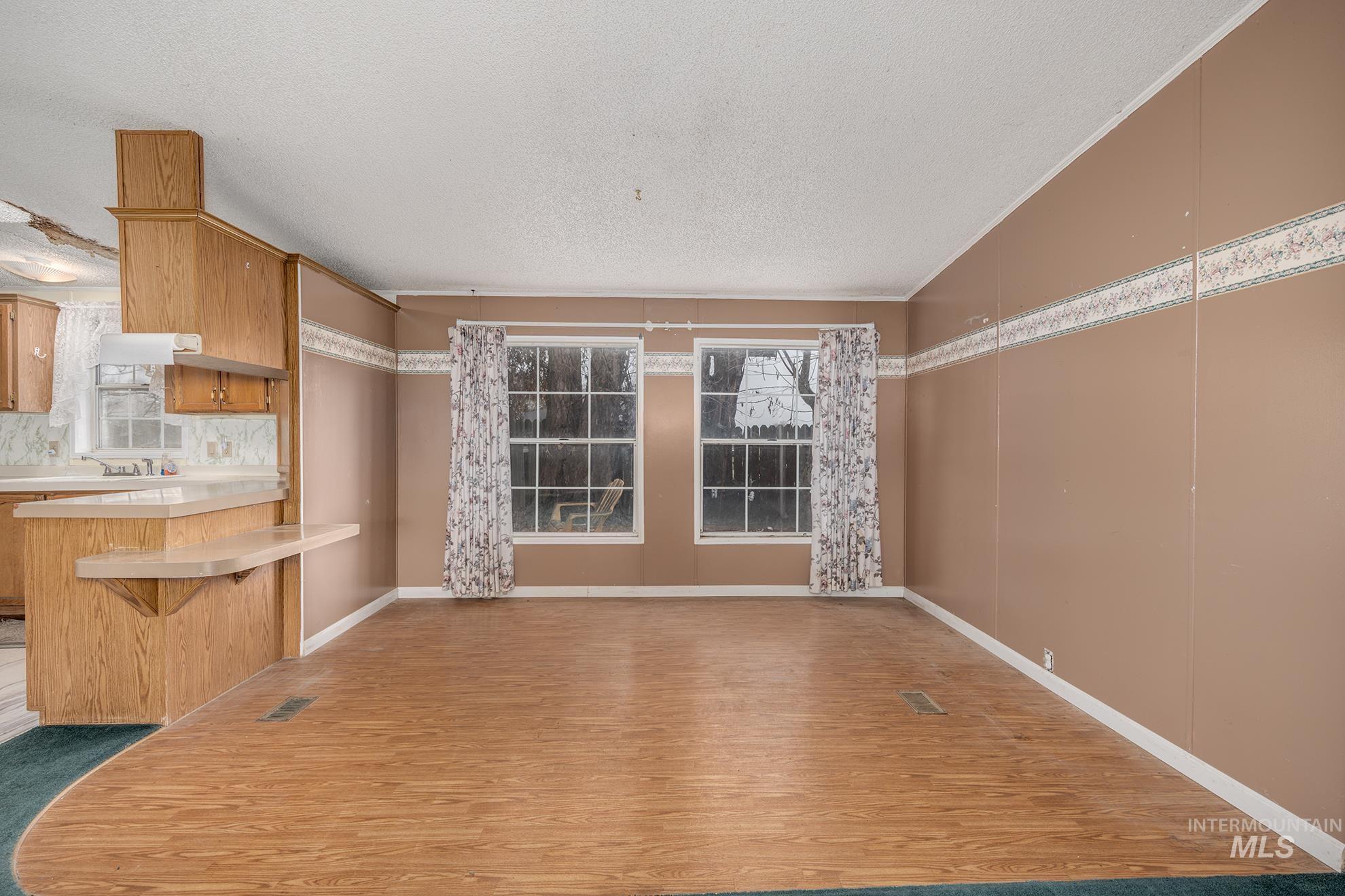 Unfurnished dining area featuring light wood-type flooring, a textured ceiling, and lofted ceiling
