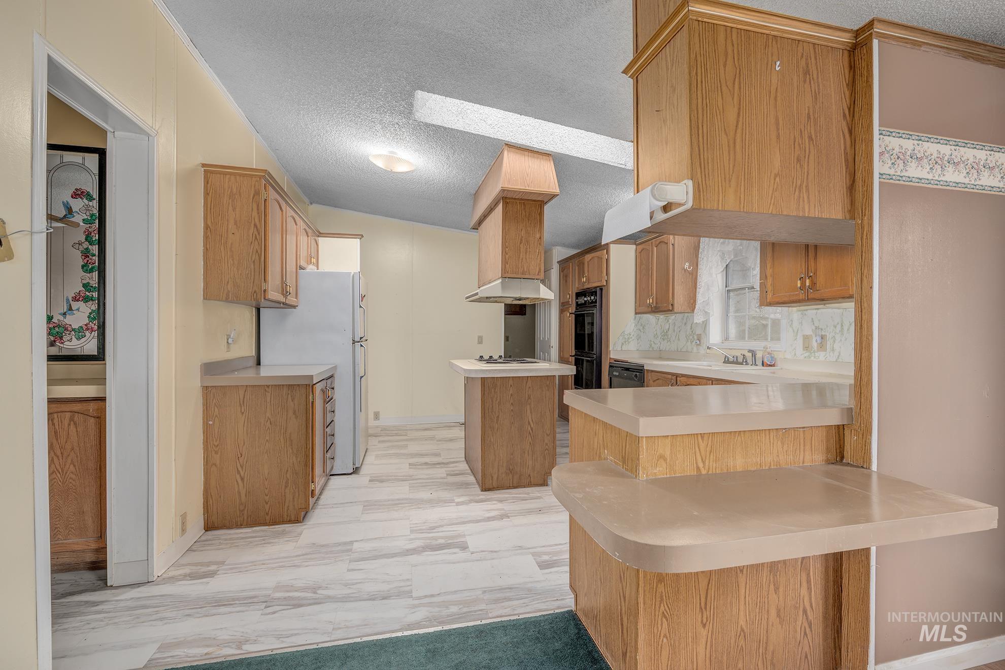 Kitchen featuring a textured ceiling, light countertops, freestanding refrigerator, a center island, and light marble finish floors