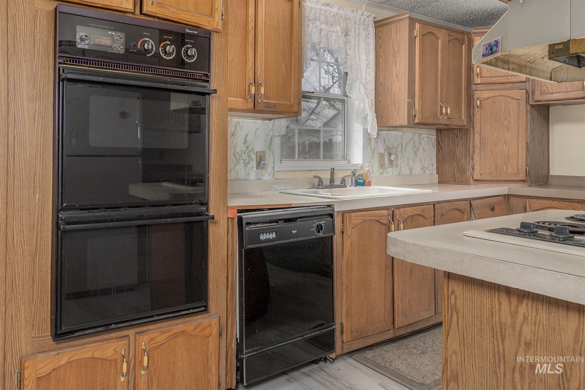 Kitchen featuring black appliances, light countertops, brown cabinets, ventilation hood, and decorative backsplash