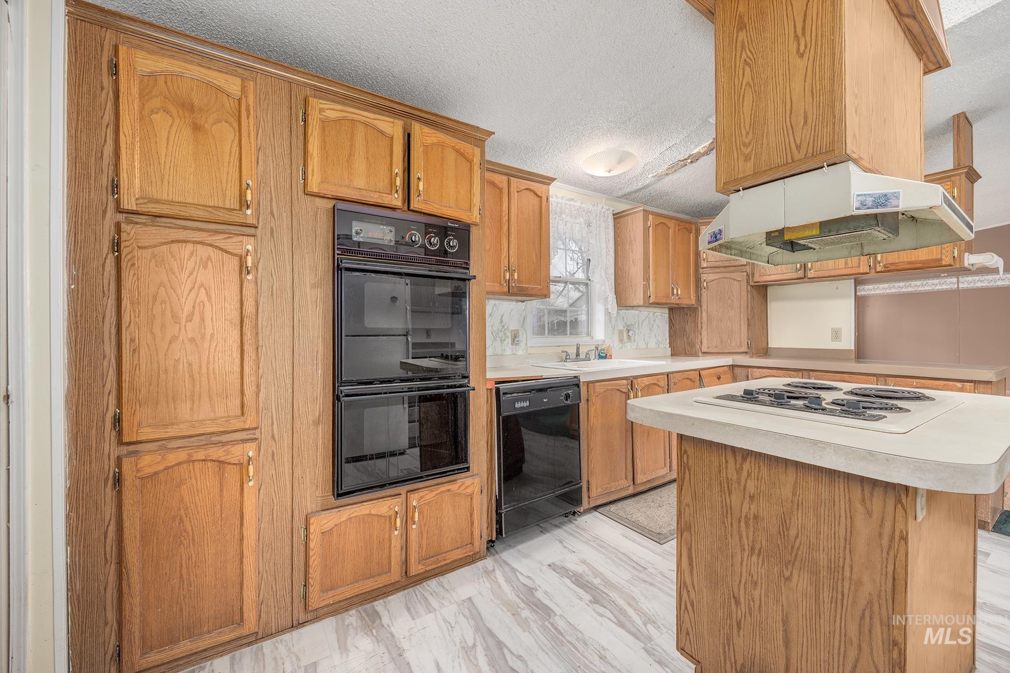 Kitchen featuring a textured ceiling, black appliances, light countertops, a kitchen island, and under cabinet range hood