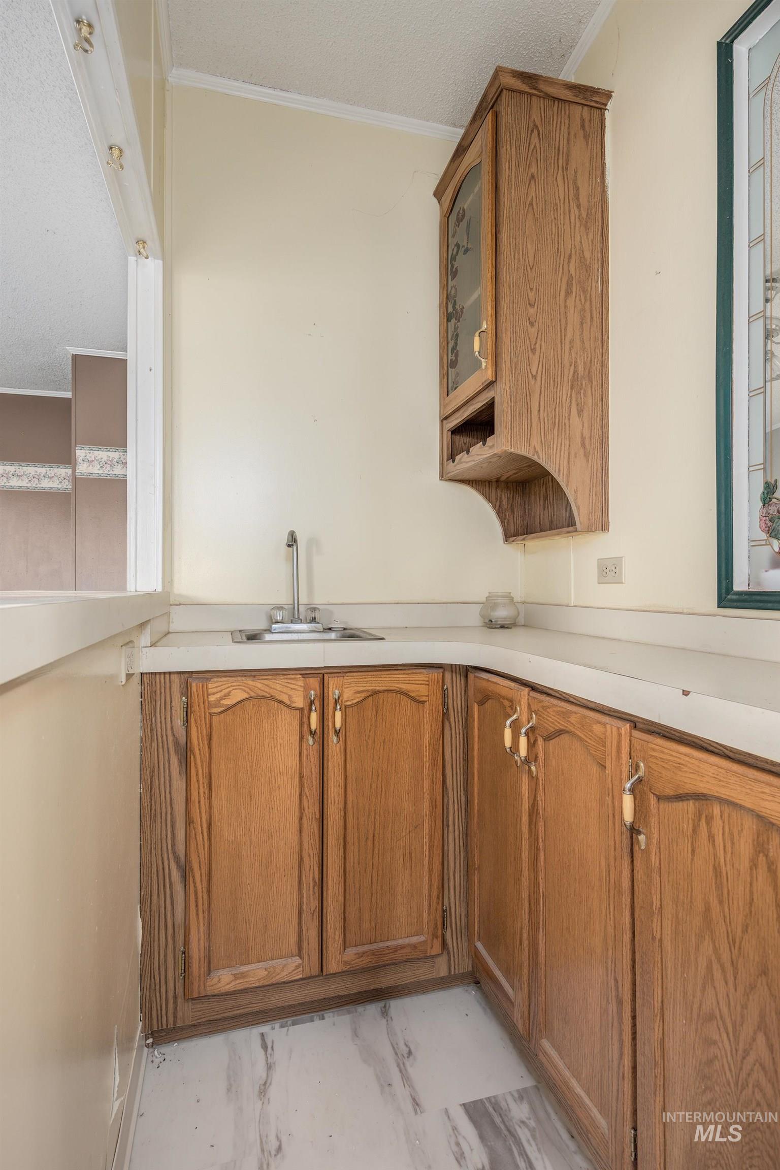 Kitchen featuring brown cabinets, glass insert cabinets, light countertops, a textured ceiling, and ornamental molding