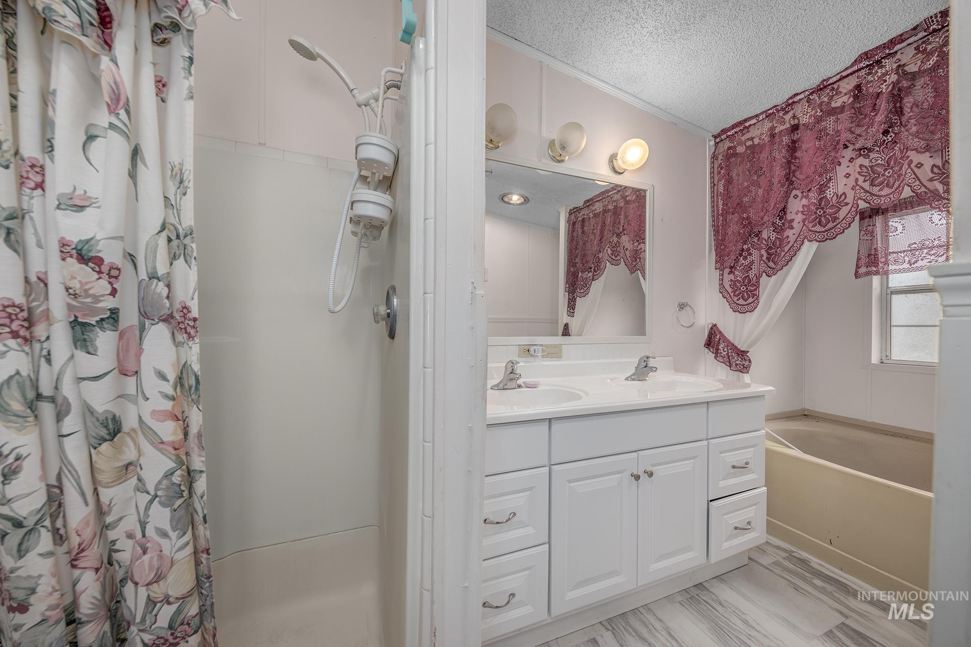 Full bath featuring double vanity, a textured ceiling, a stall shower, and a bath