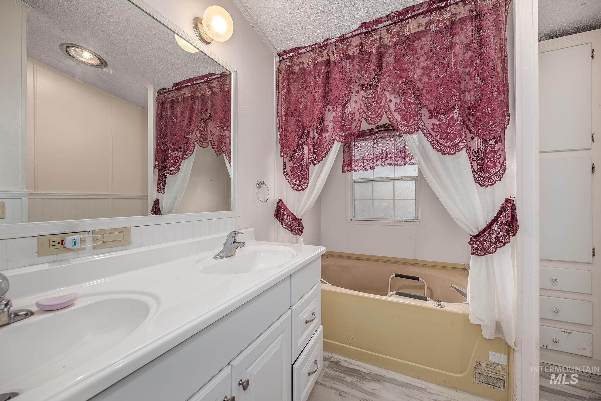 Bathroom with a textured ceiling, double vanity, and a bath
