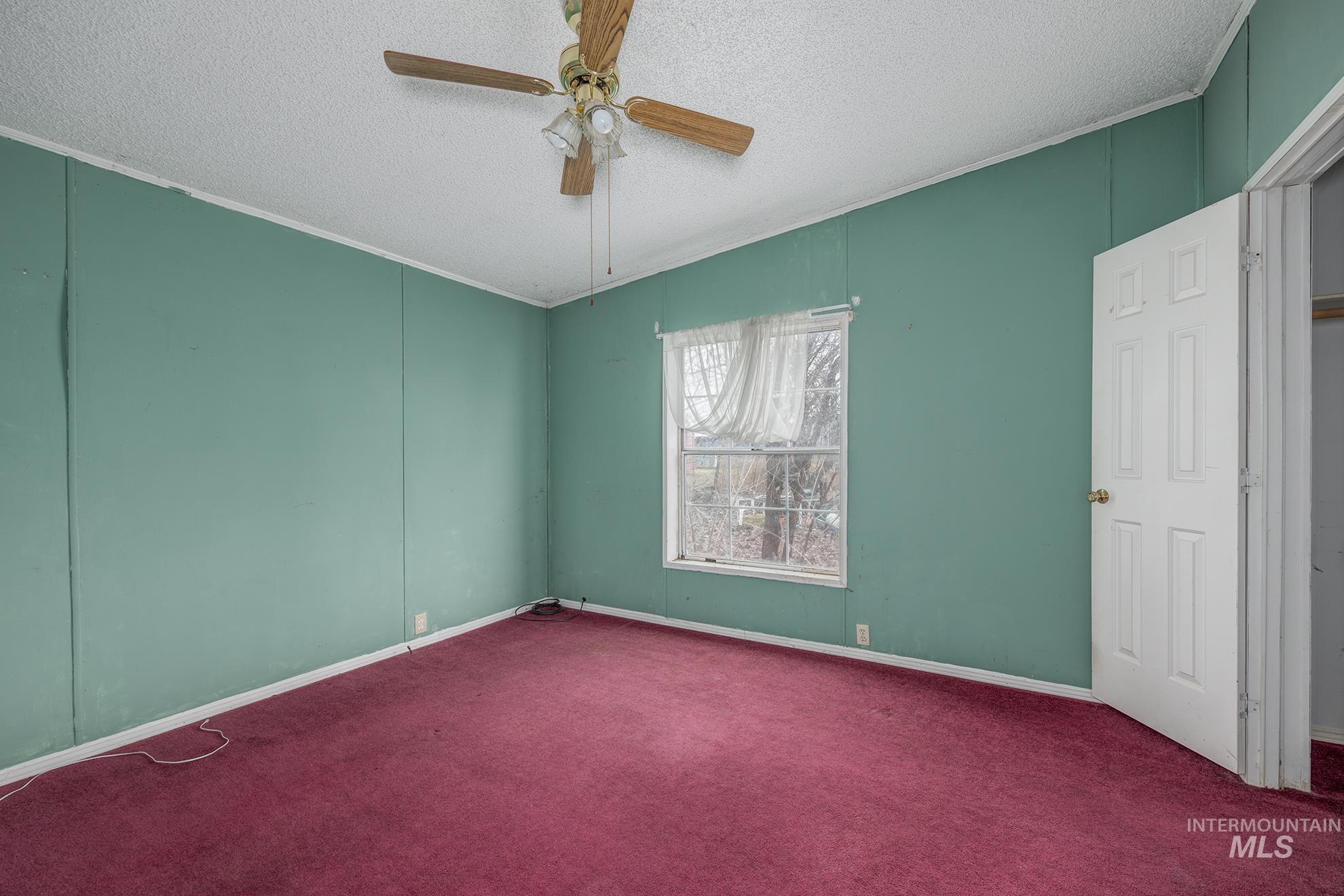 Carpeted empty room featuring a textured ceiling, a ceiling fan, and a decorative wall
