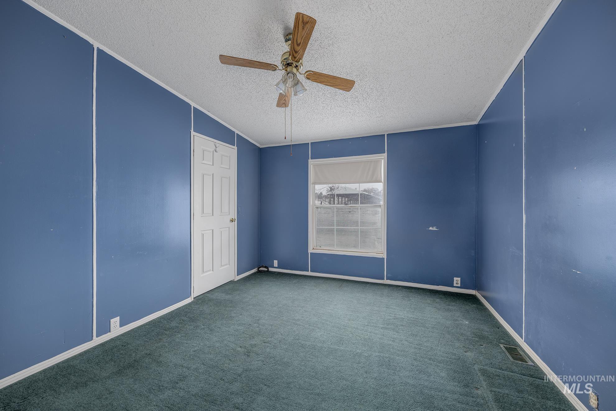 Carpeted empty room featuring a textured ceiling, ceiling fan, and ornamental molding
