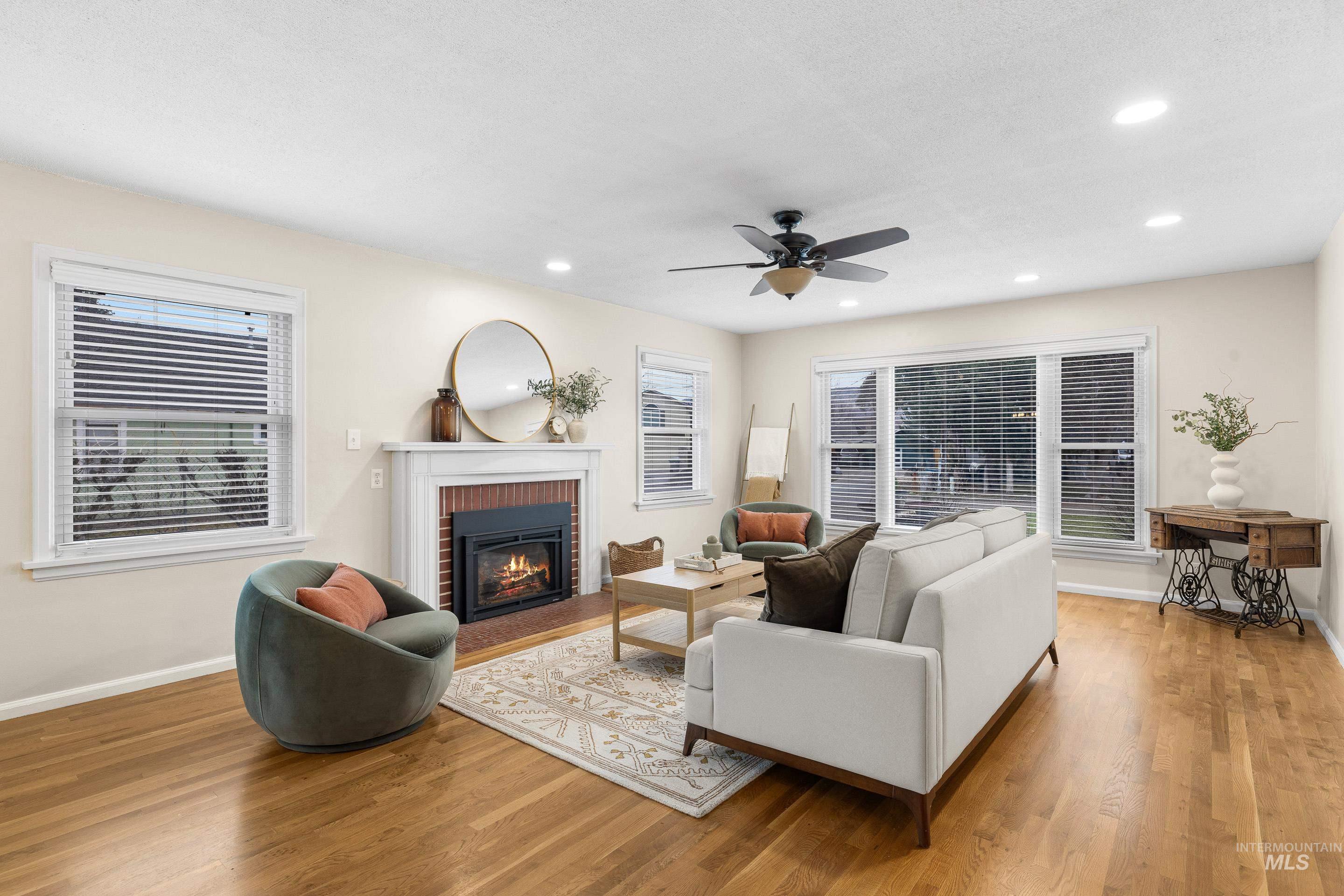 Living room with a brick fireplace, light wood-type flooring, plenty of natural light, and recessed lighting