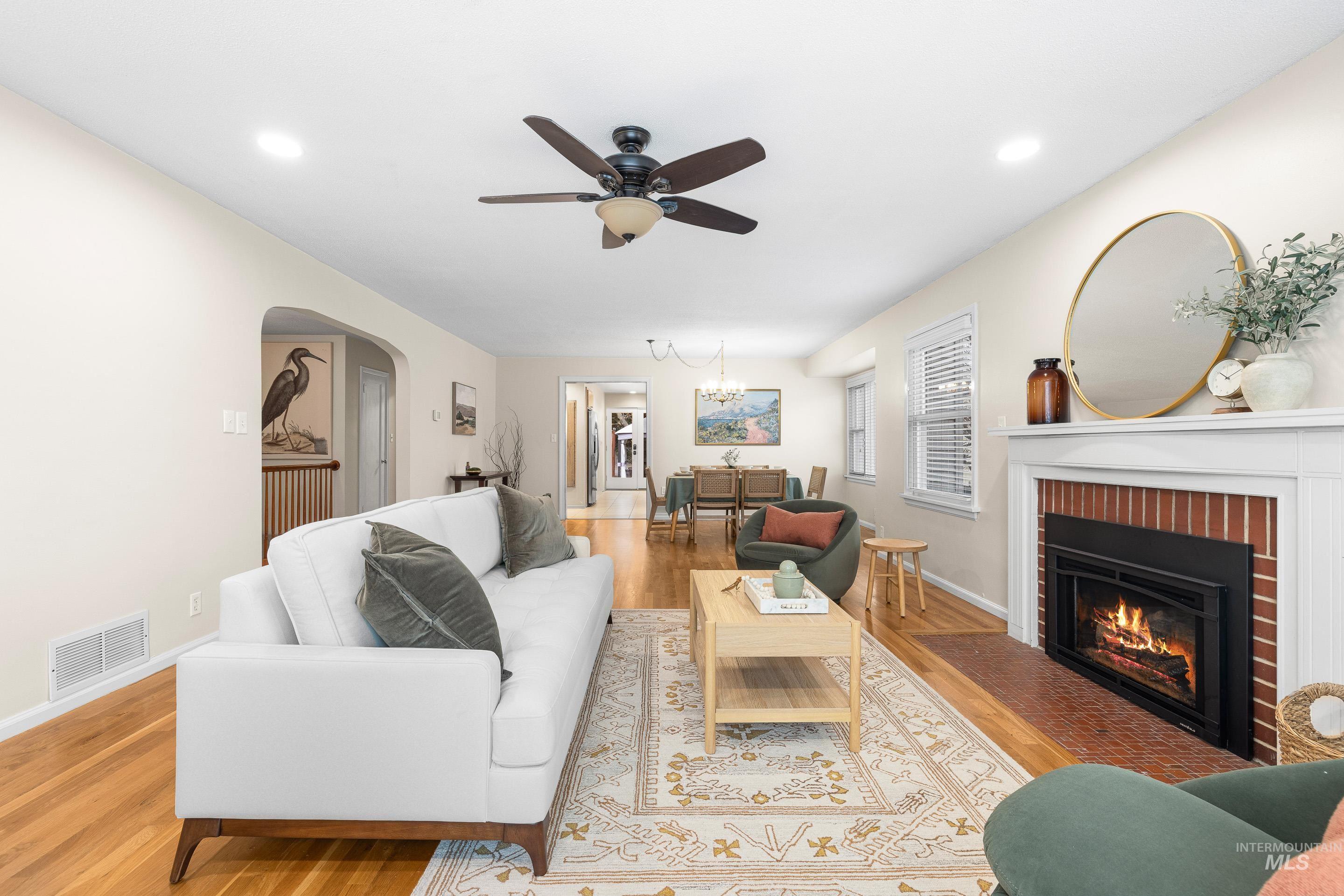 Living area featuring wood finished floors, a chandelier, a fireplace, arched walkways, and ceiling fan