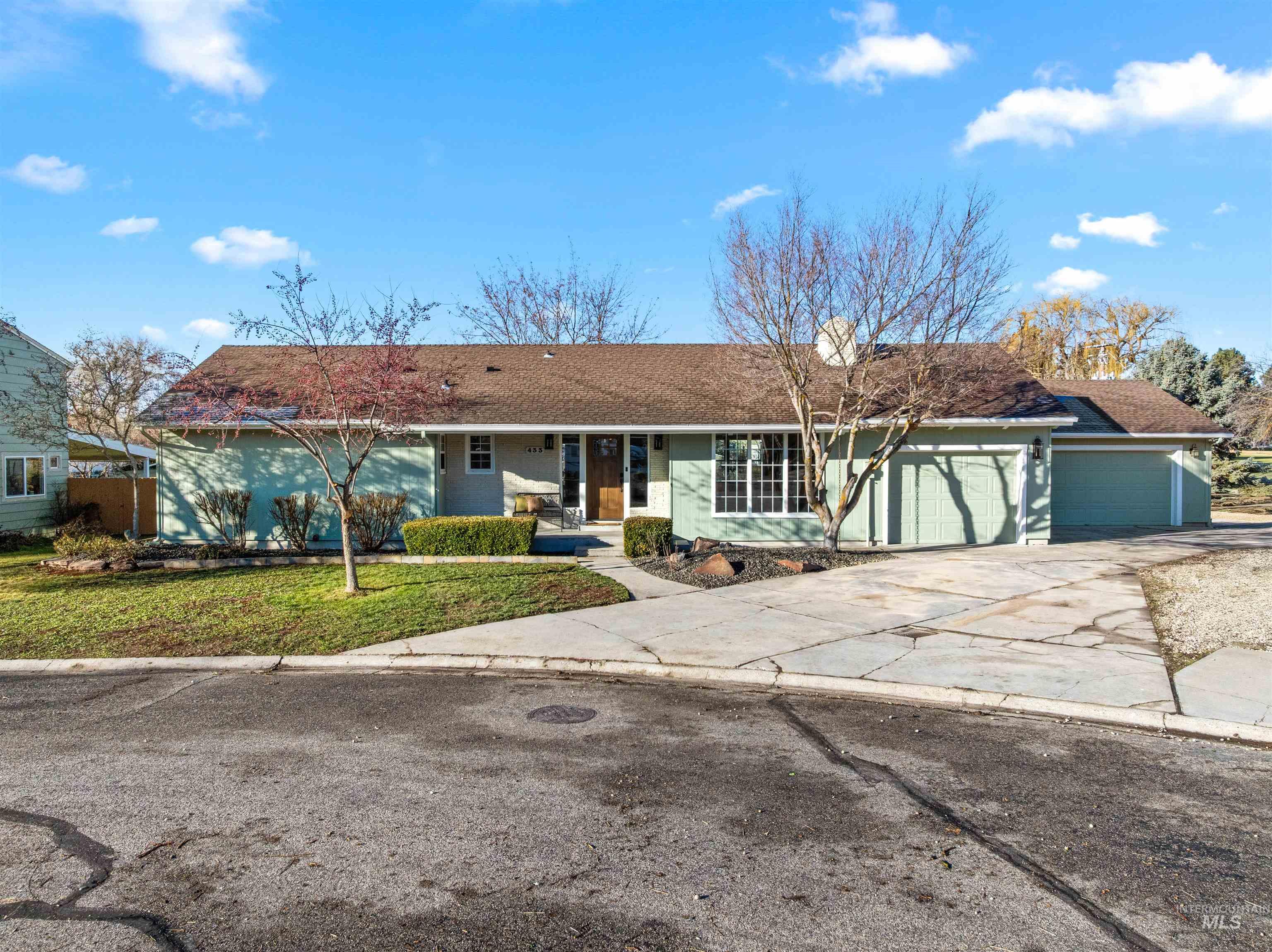 Single story home featuring driveway, a garage, a front yard, a shingled roof, and covered porch