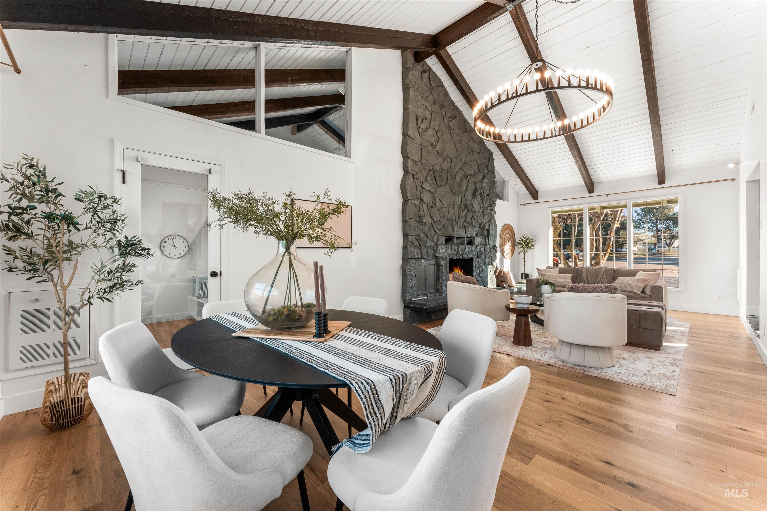 Dining space featuring a stone fireplace, high vaulted ceiling, light wood-style flooring, a chandelier, and a wooden ceiling with exposed beams