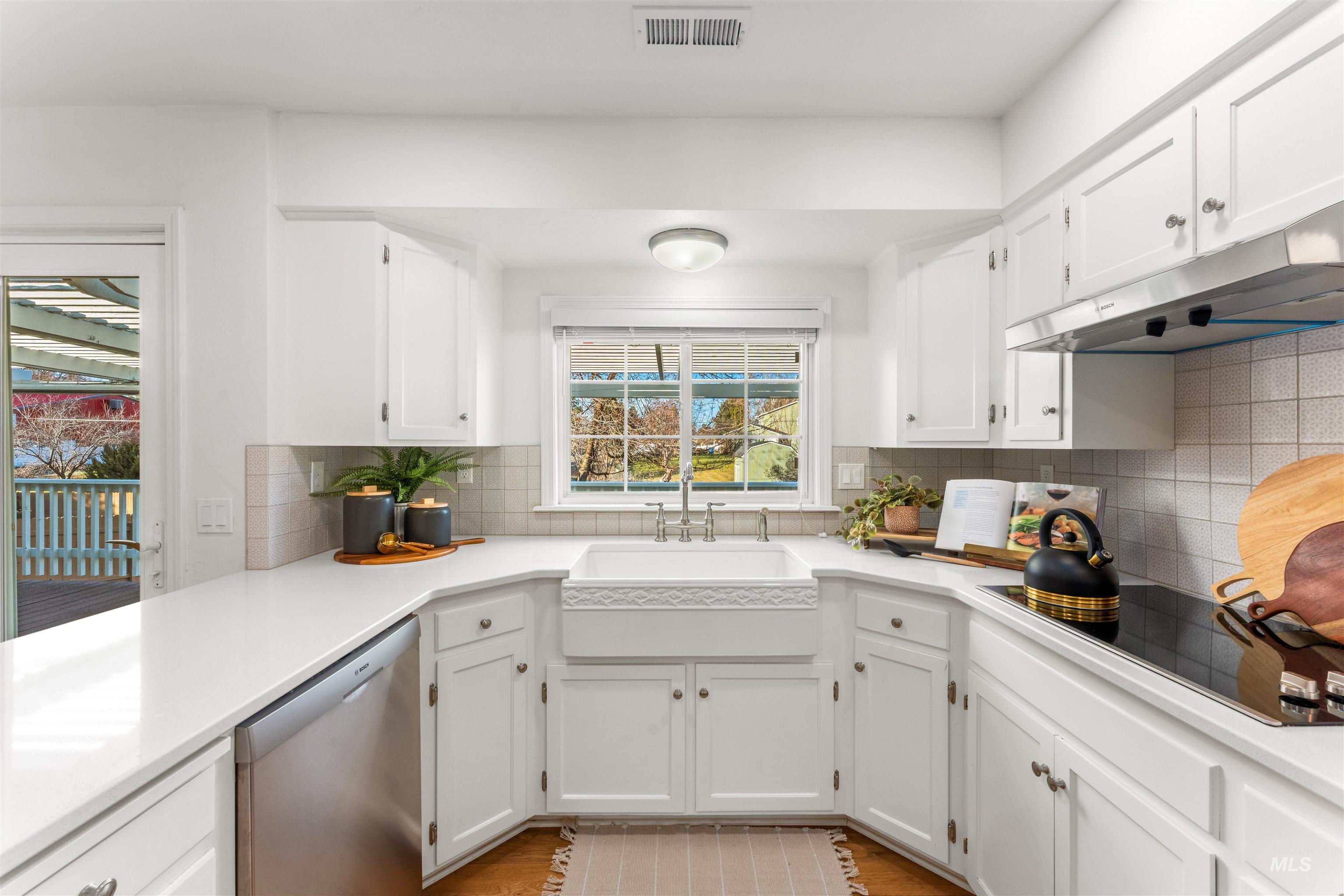 Kitchen with white cabinetry, stainless steel dishwasher, black electric cooktop, under cabinet range hood, and decorative backsplash