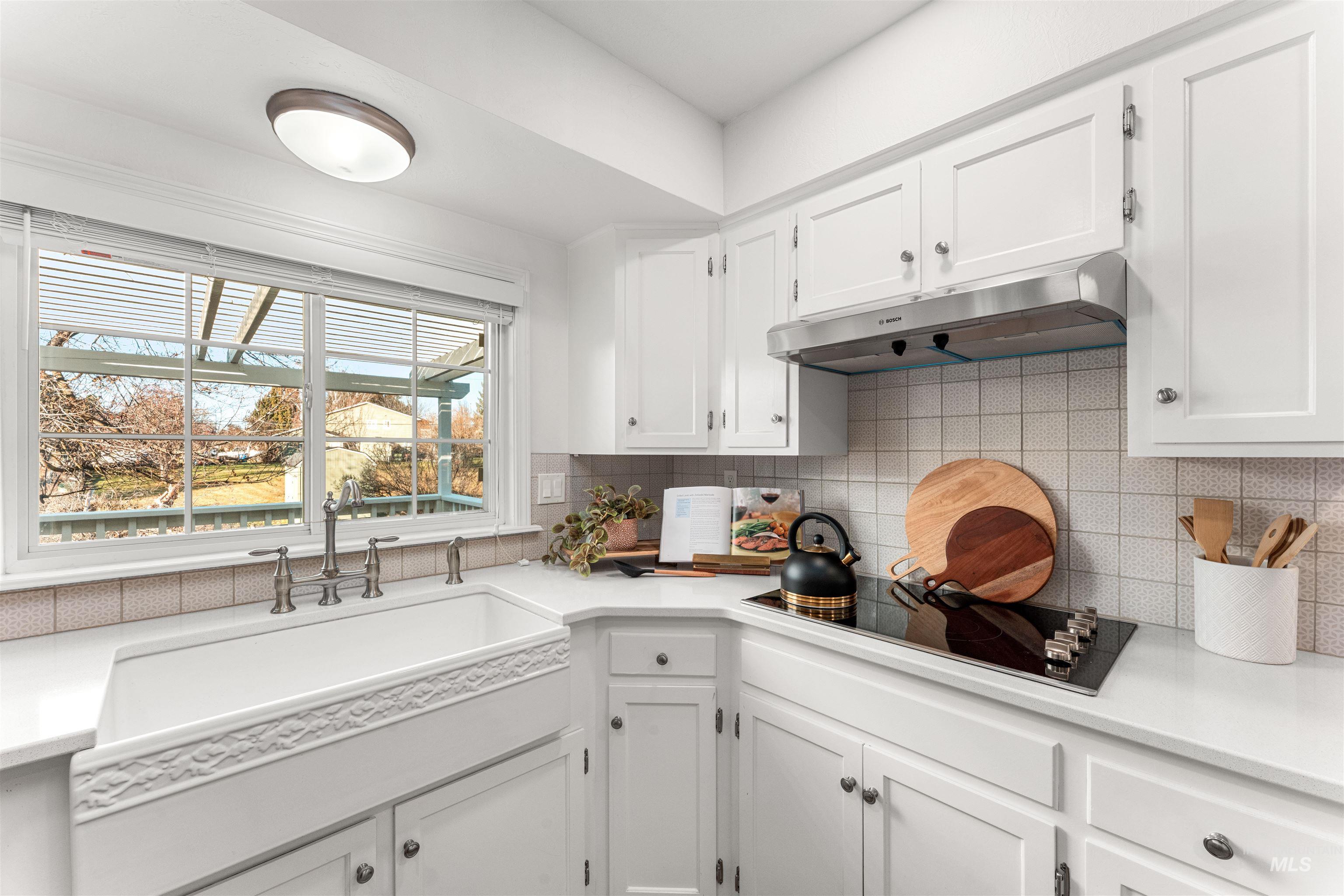 Kitchen featuring white cabinetry, under cabinet range hood, tasteful backsplash, and black electric cooktop