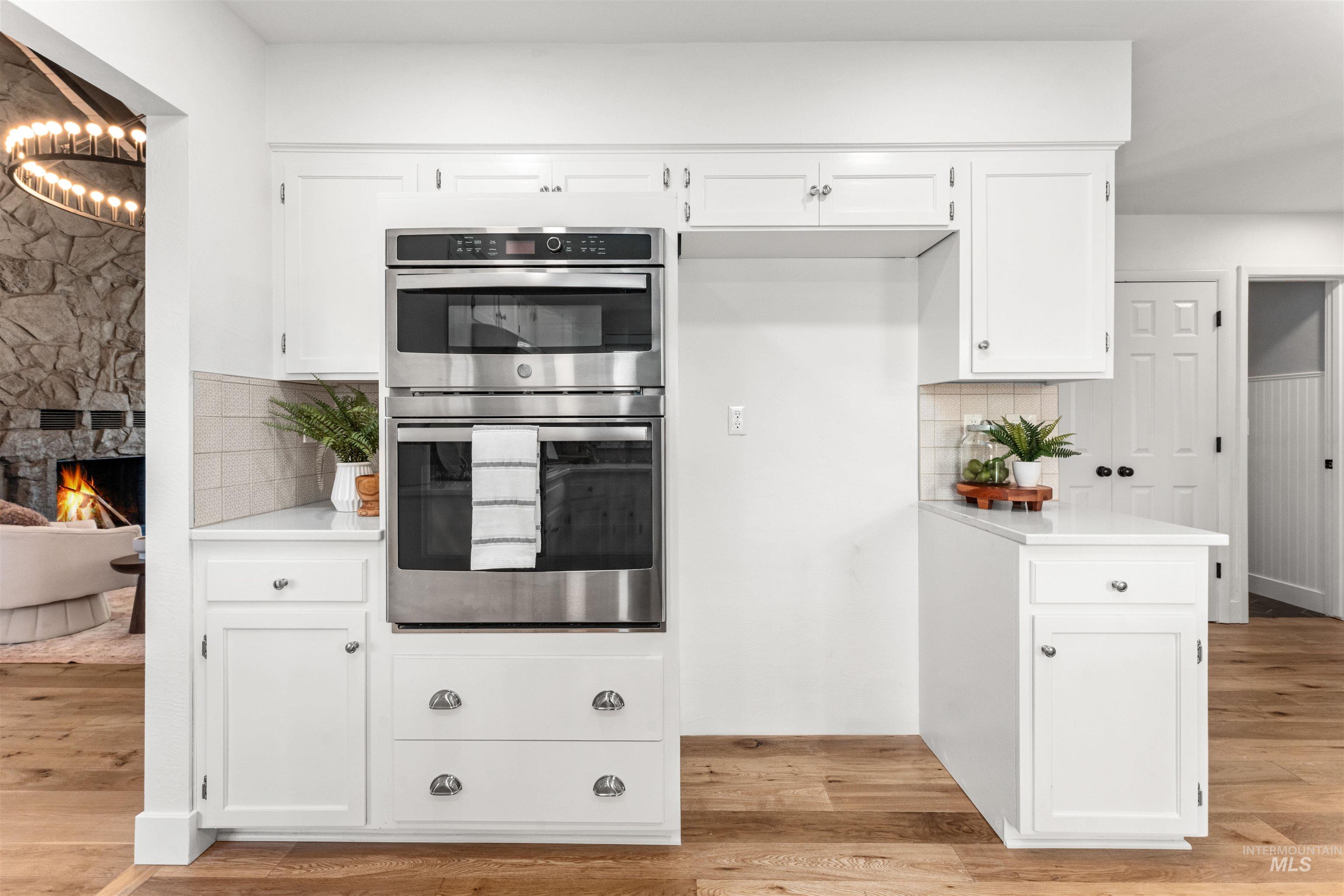 Kitchen featuring stainless steel double oven, white cabinetry, light wood finished floors, and a fireplace