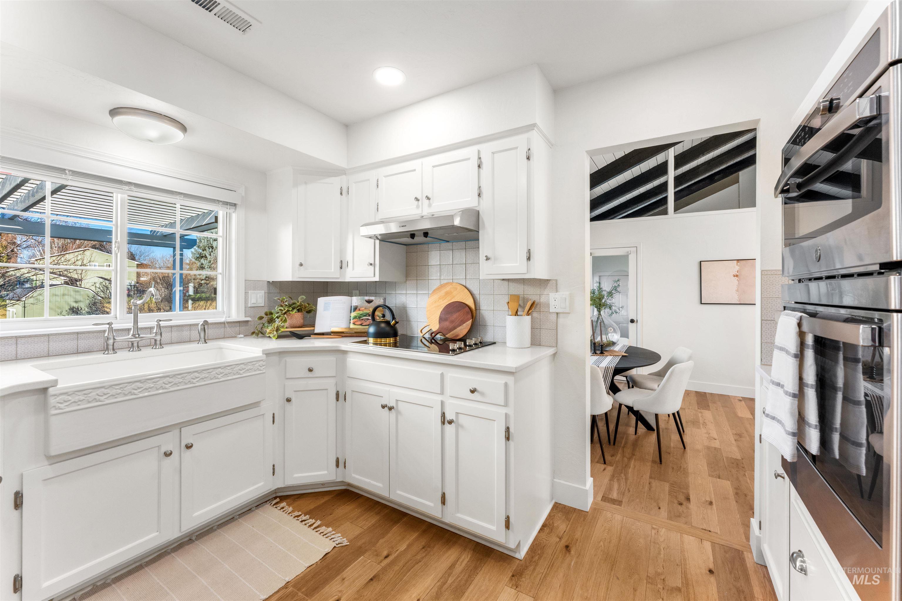Kitchen featuring double oven, white cabinetry, light wood-style flooring, beam ceiling, and backsplash