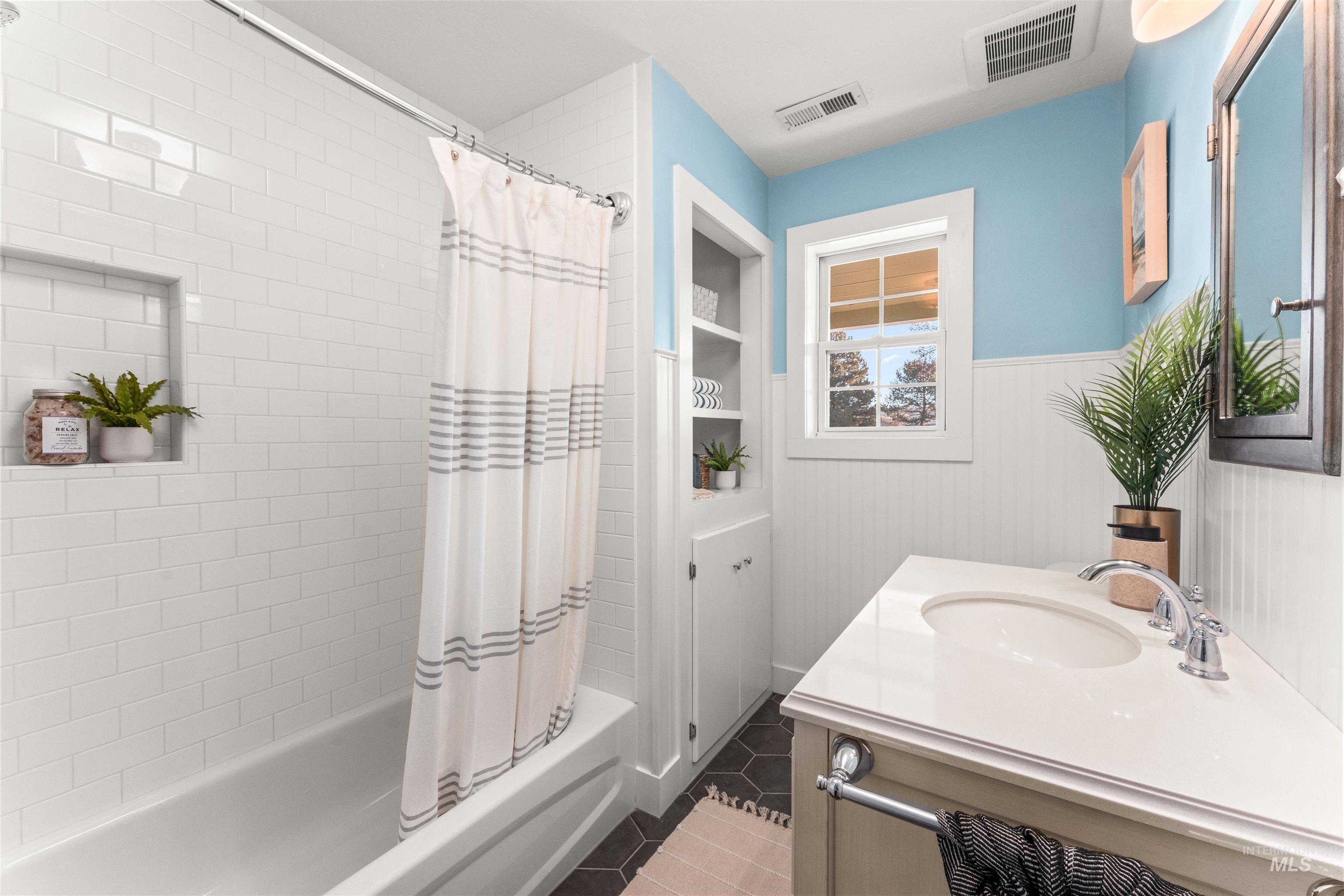 Bathroom with wainscoting, shower / tub combo, vanity, dark tile patterned flooring, and built in shelves
