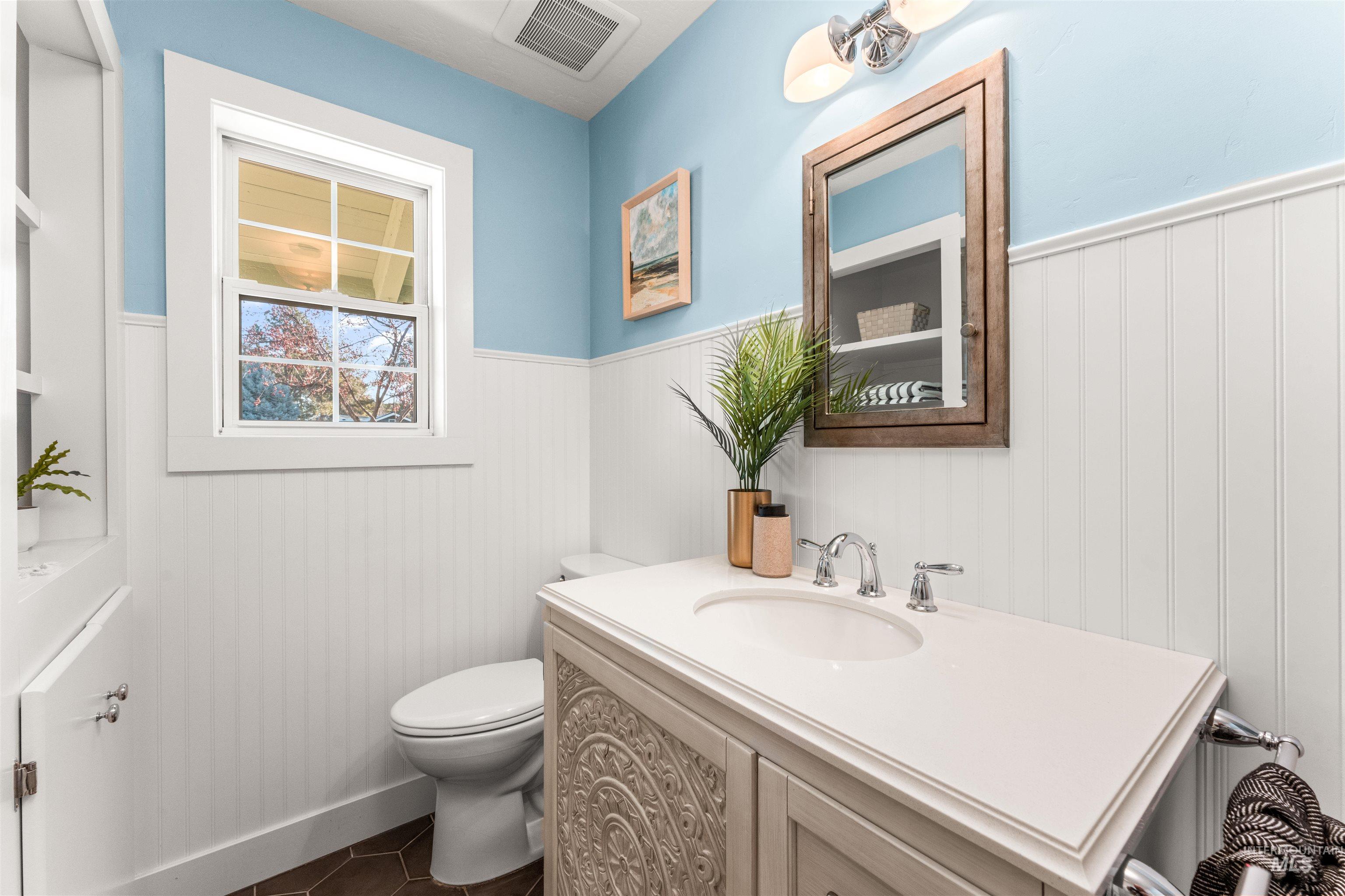 Half bath with a wainscoted wall, vanity, and dark tile patterned flooring
