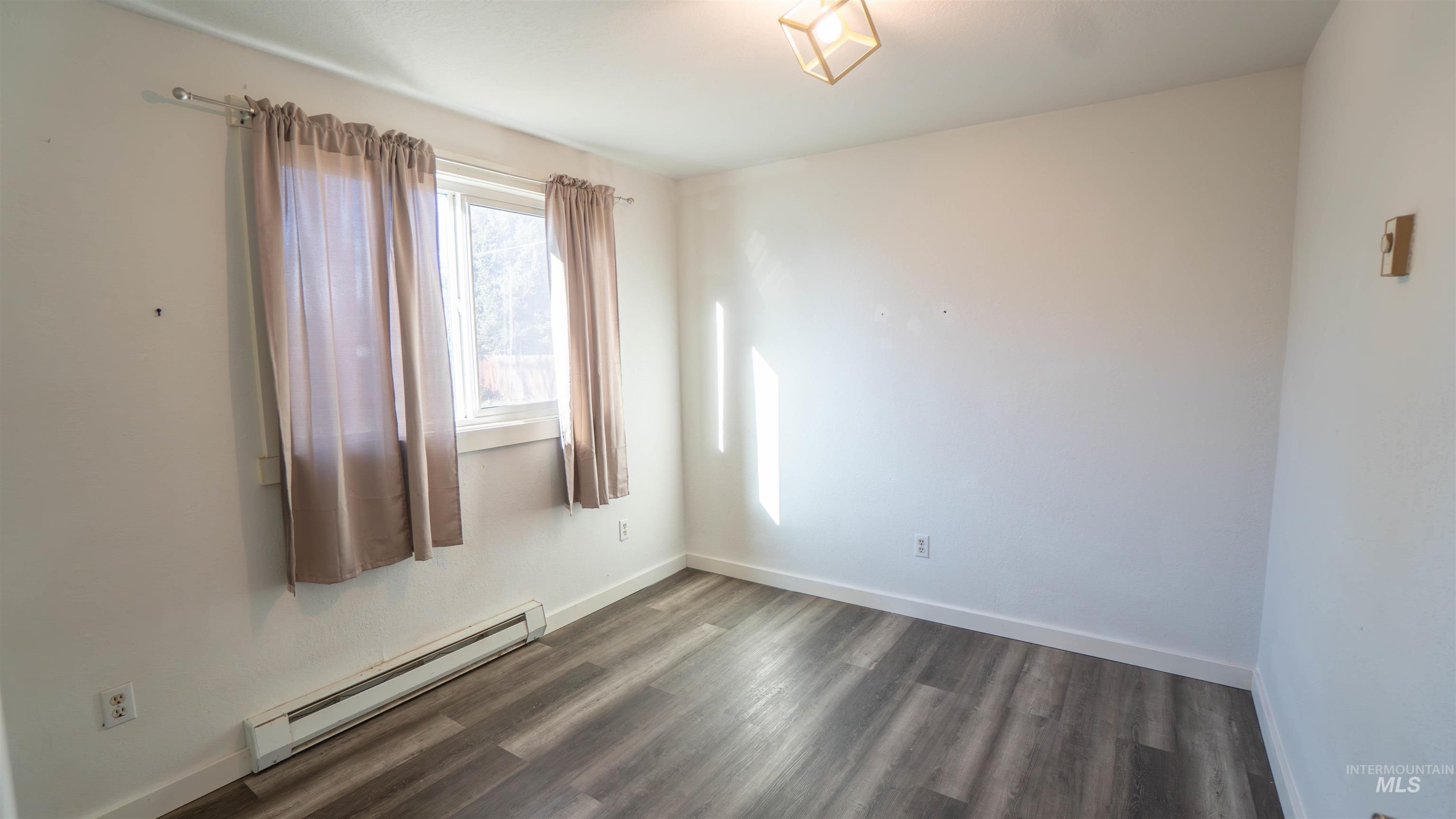 Spare room with a baseboard heating unit and dark wood-type flooring