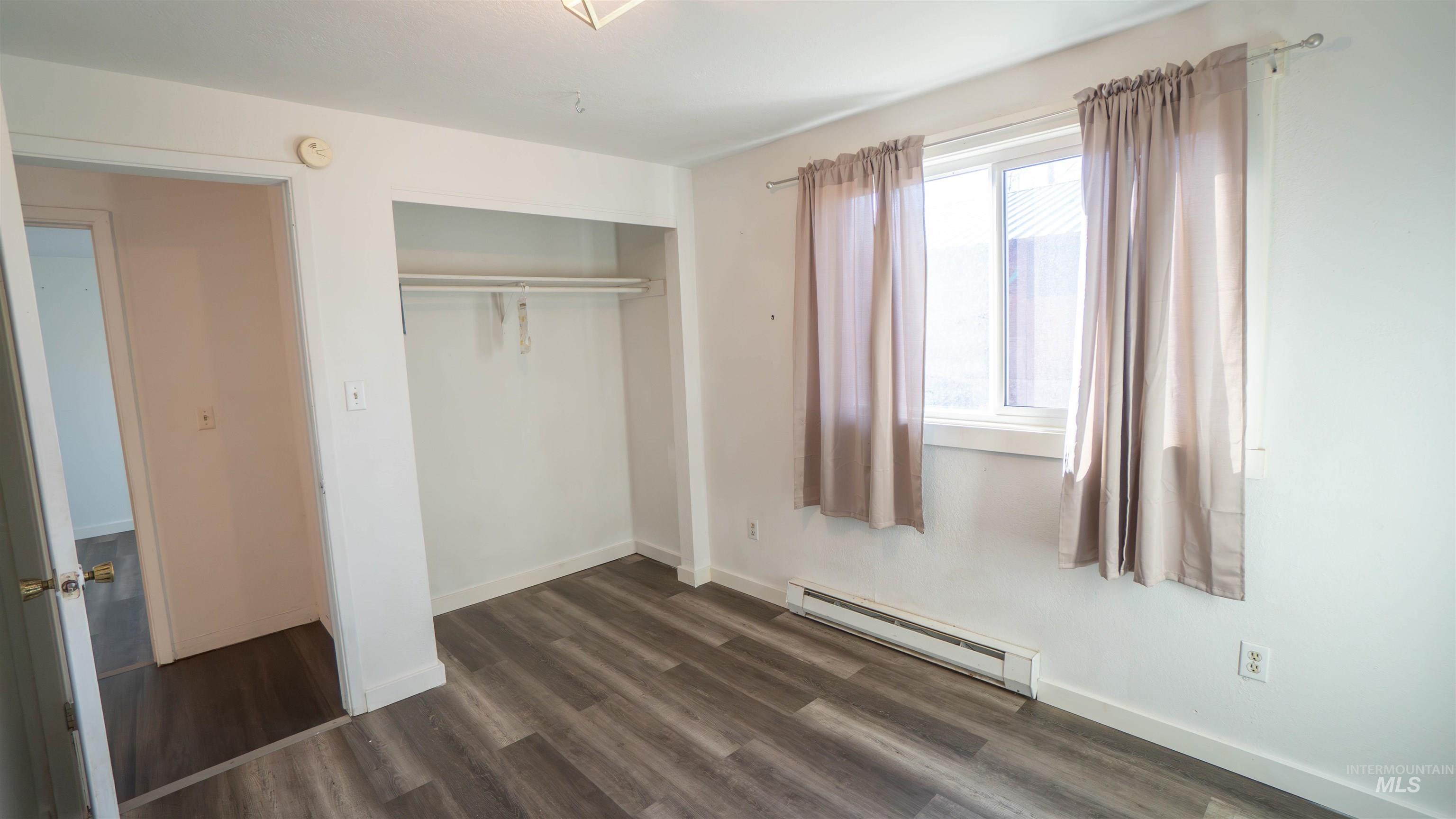 Unfurnished bedroom with a baseboard heating unit, a closet, and dark wood finished floors