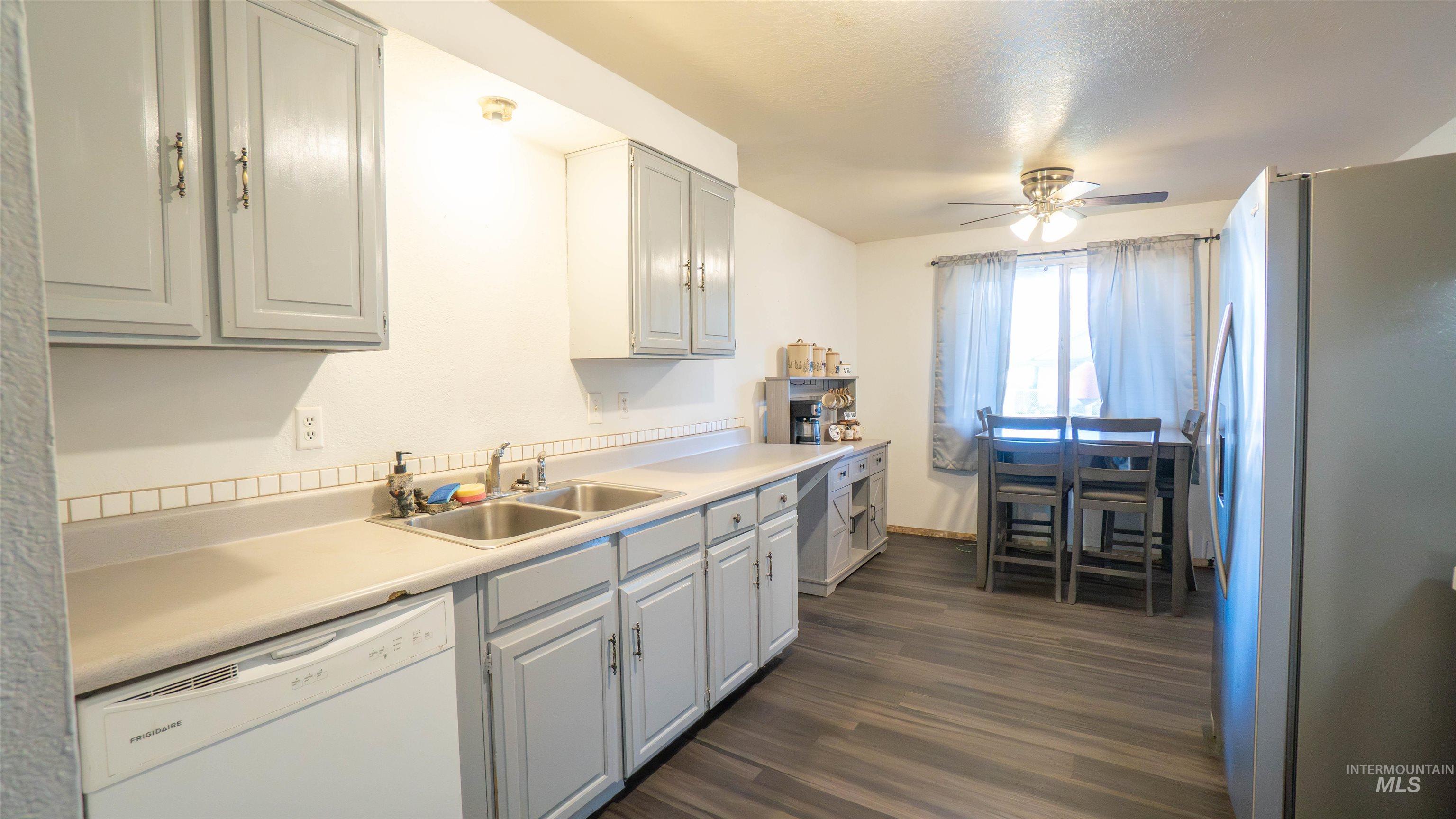 Kitchen featuring freestanding refrigerator, light countertops, white dishwasher, dark wood-style floors, and ceiling fan
