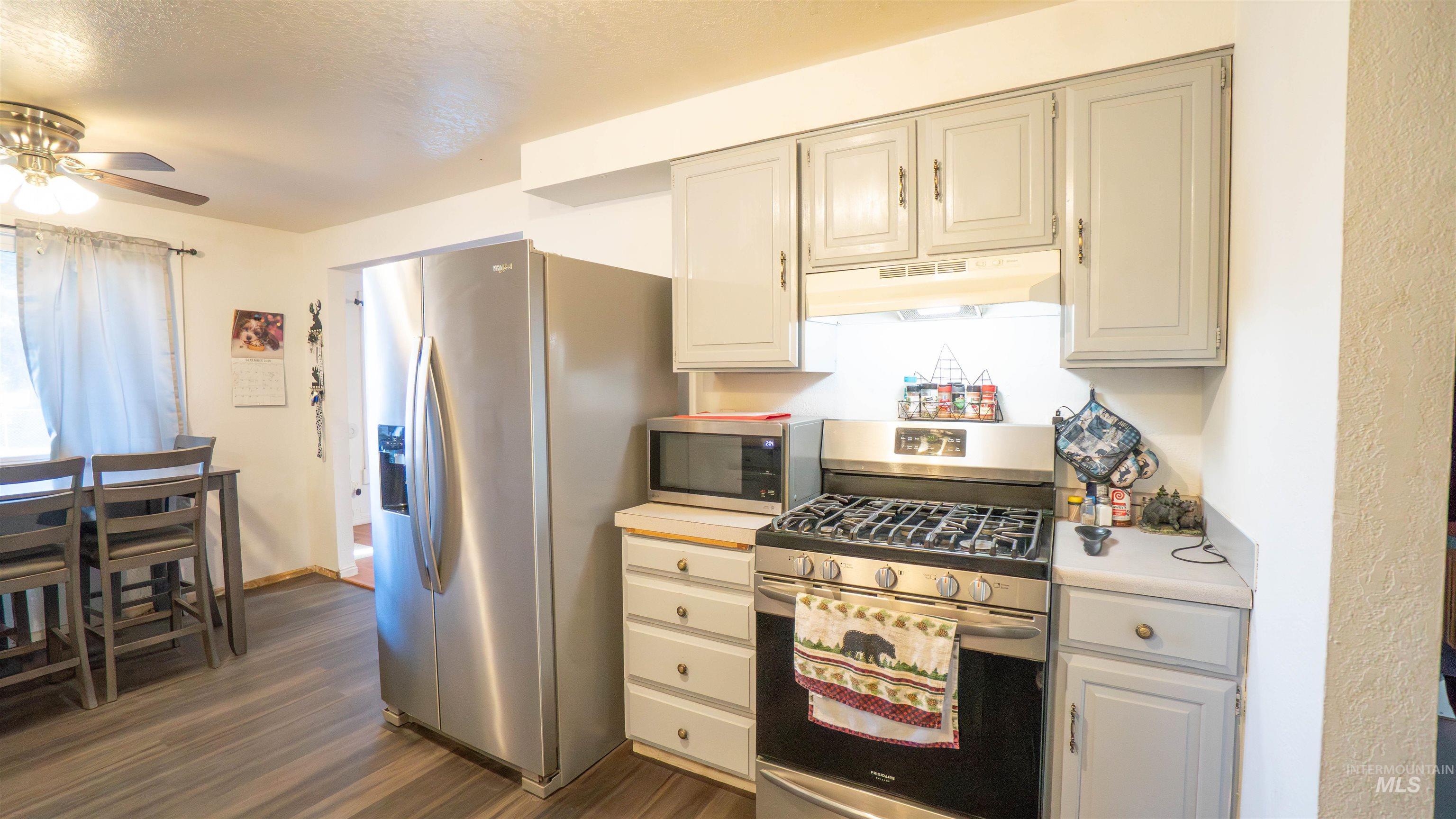 Kitchen with appliances with stainless steel finishes, light countertops, dark wood-style flooring, under cabinet range hood, and a textured ceiling