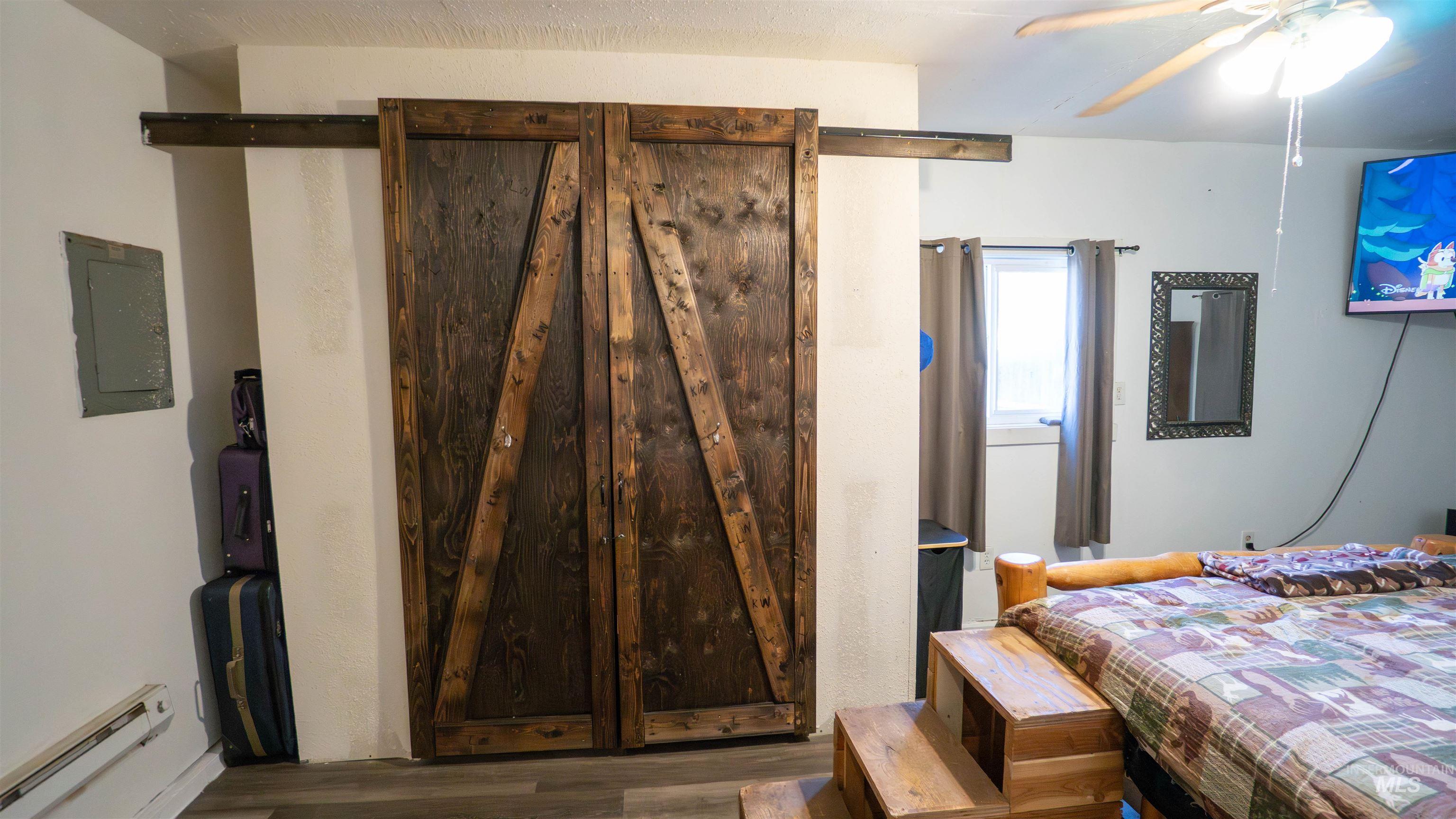 Bedroom with a baseboard radiator, wood finished floors, electric panel, and ceiling fan