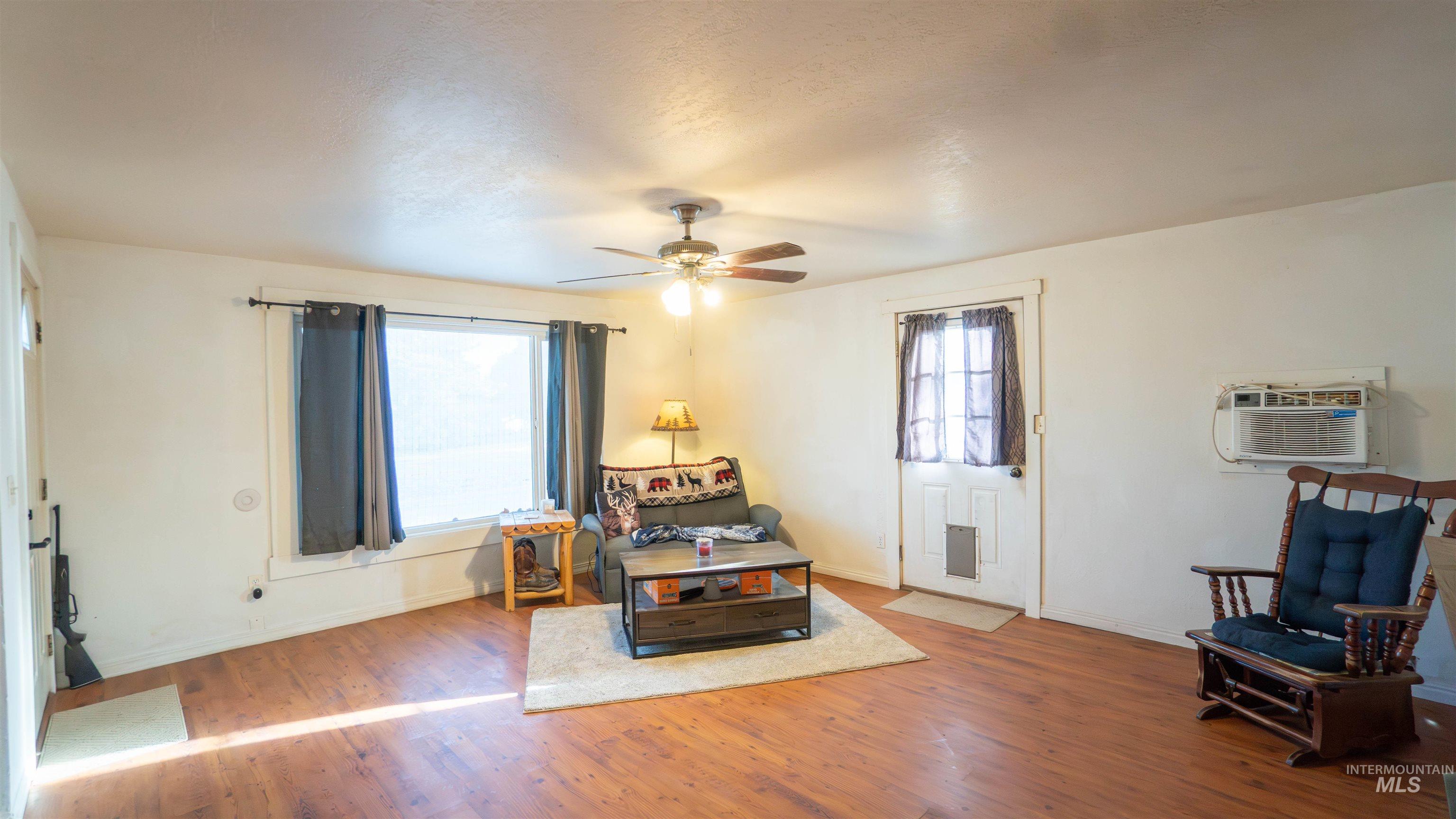 Living area with wood finished floors, a wall unit AC, and ceiling fan