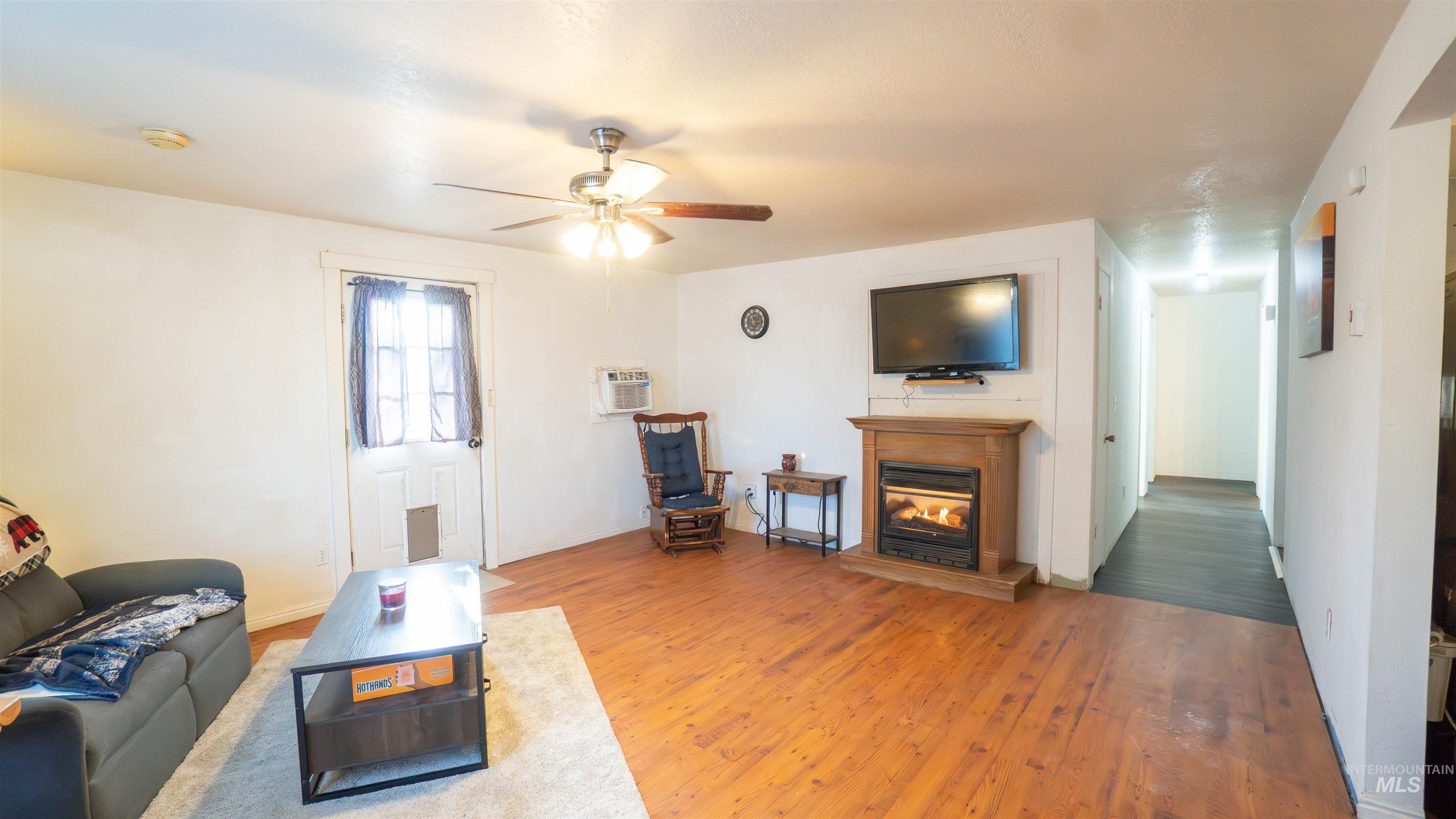 Living room featuring a glass covered fireplace, light wood-style floors, ceiling fan, and a wall mounted AC