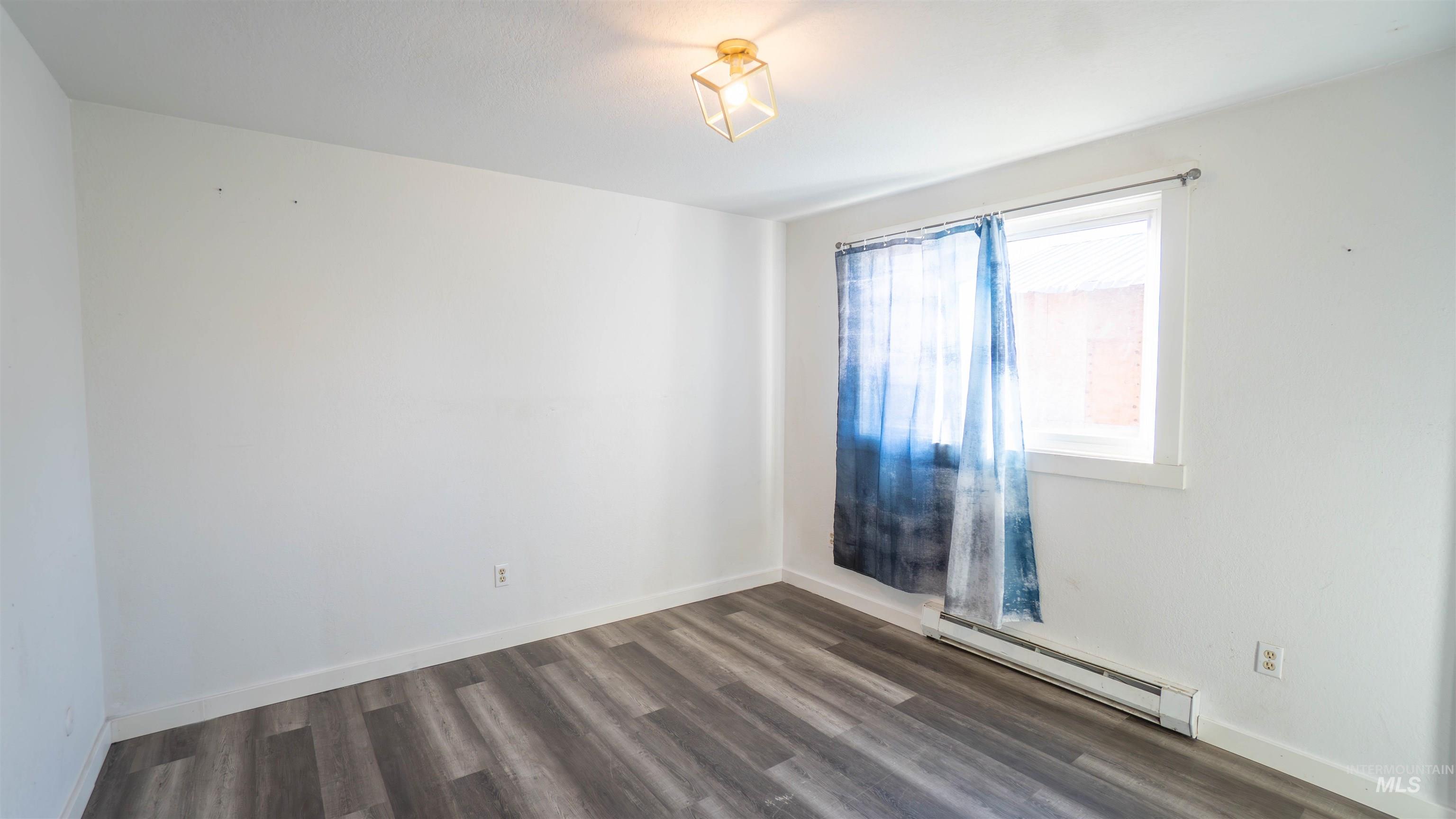 Empty room with a baseboard heating unit and dark wood-type flooring