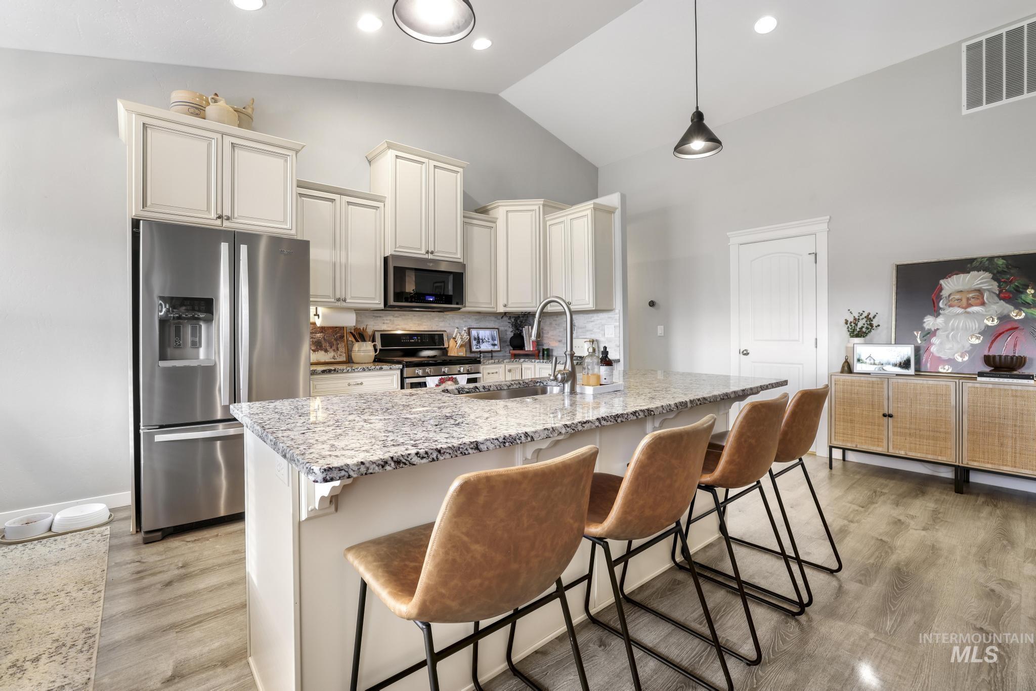 Kitchen with light stone counters, appliances with stainless steel finishes, a breakfast bar, an island with sink, and recessed lighting