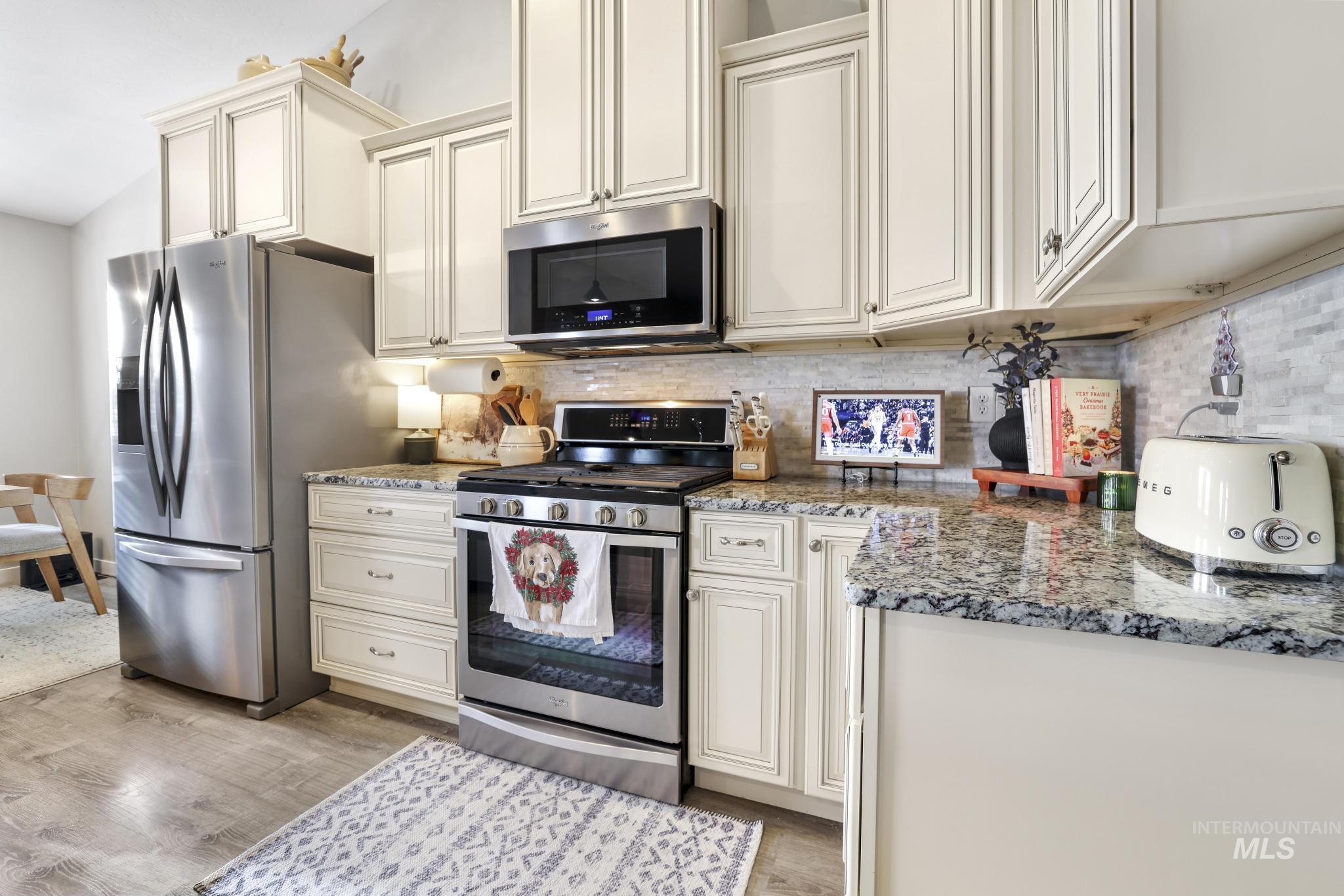 Kitchen featuring appliances with stainless steel finishes, light stone countertops, cream cabinets, decorative backsplash, and light wood-style floors
